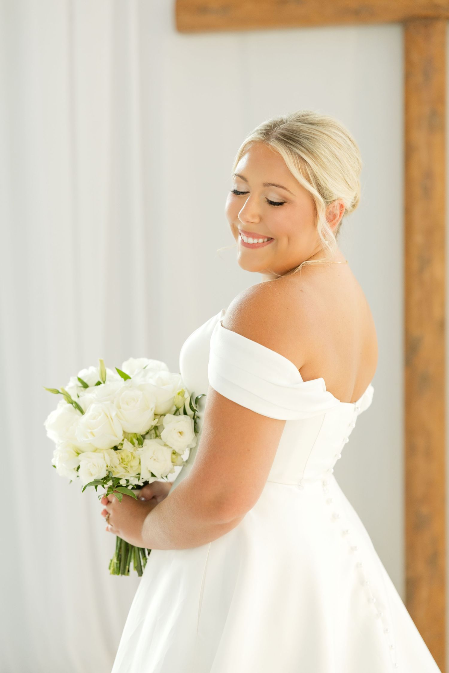 Beautiful bride in white dress holding elegant white floral bouquet during wedding preparations.