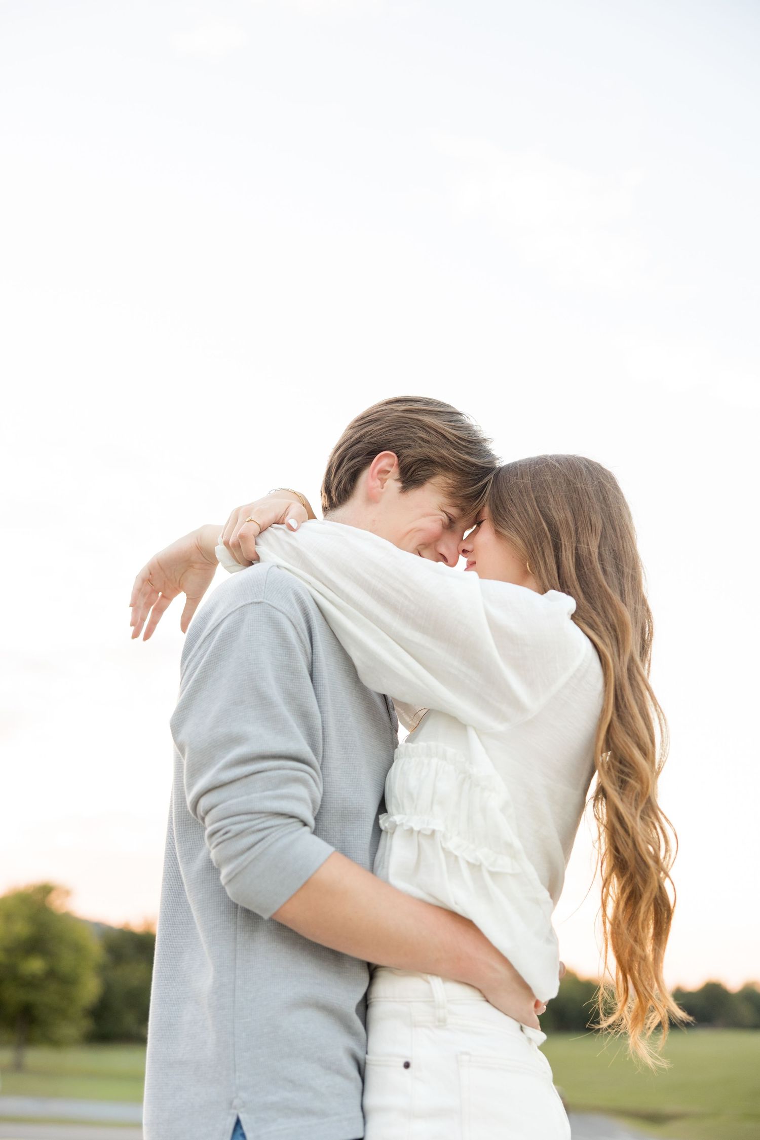 A tender embrace between a couple wearing coordinating gray and white outfits in an outdoor setting.