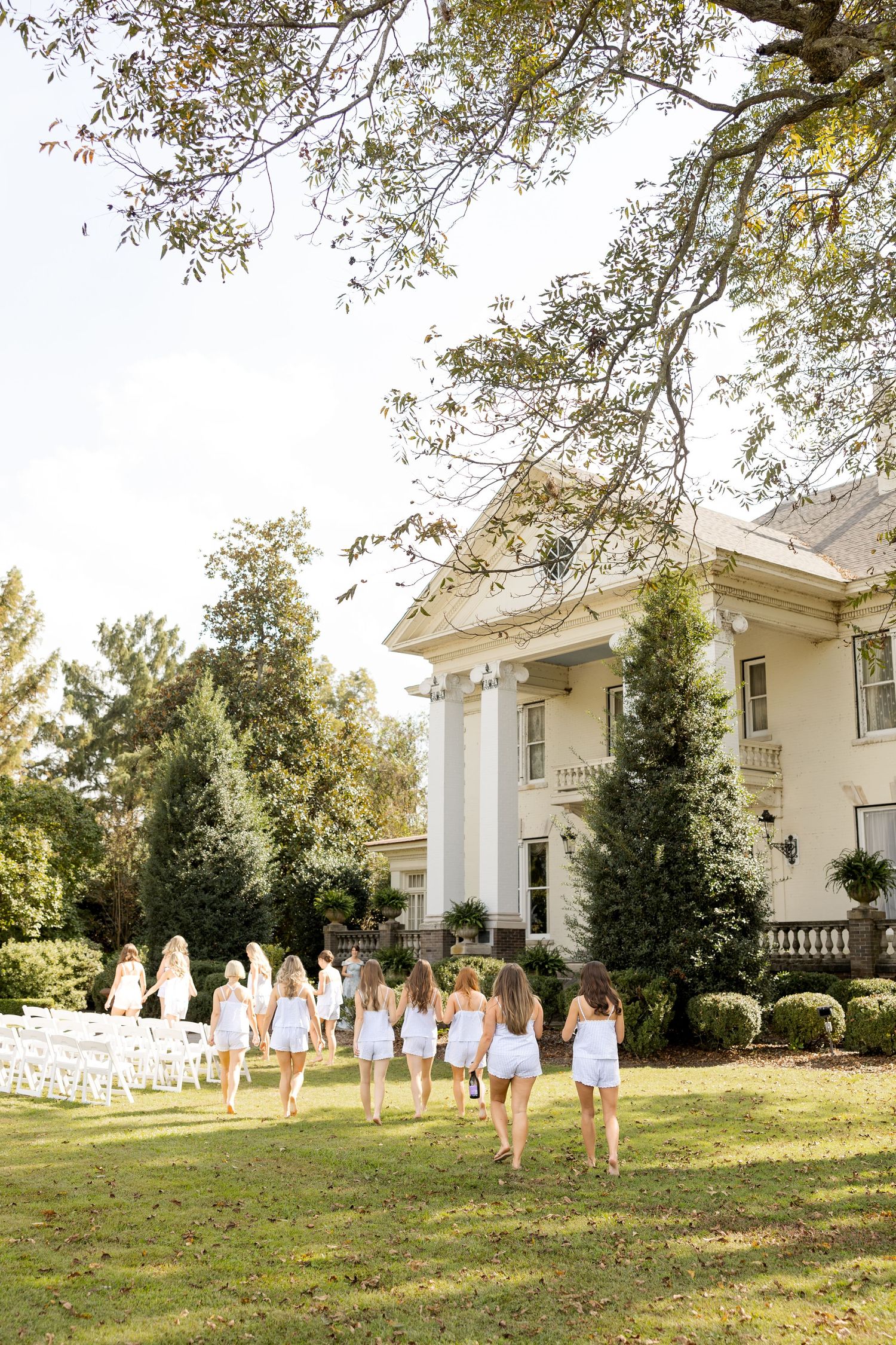 Bridesmaids in white dresses walking on lawn in front of grand southern mansion.Marlgsate Plantation