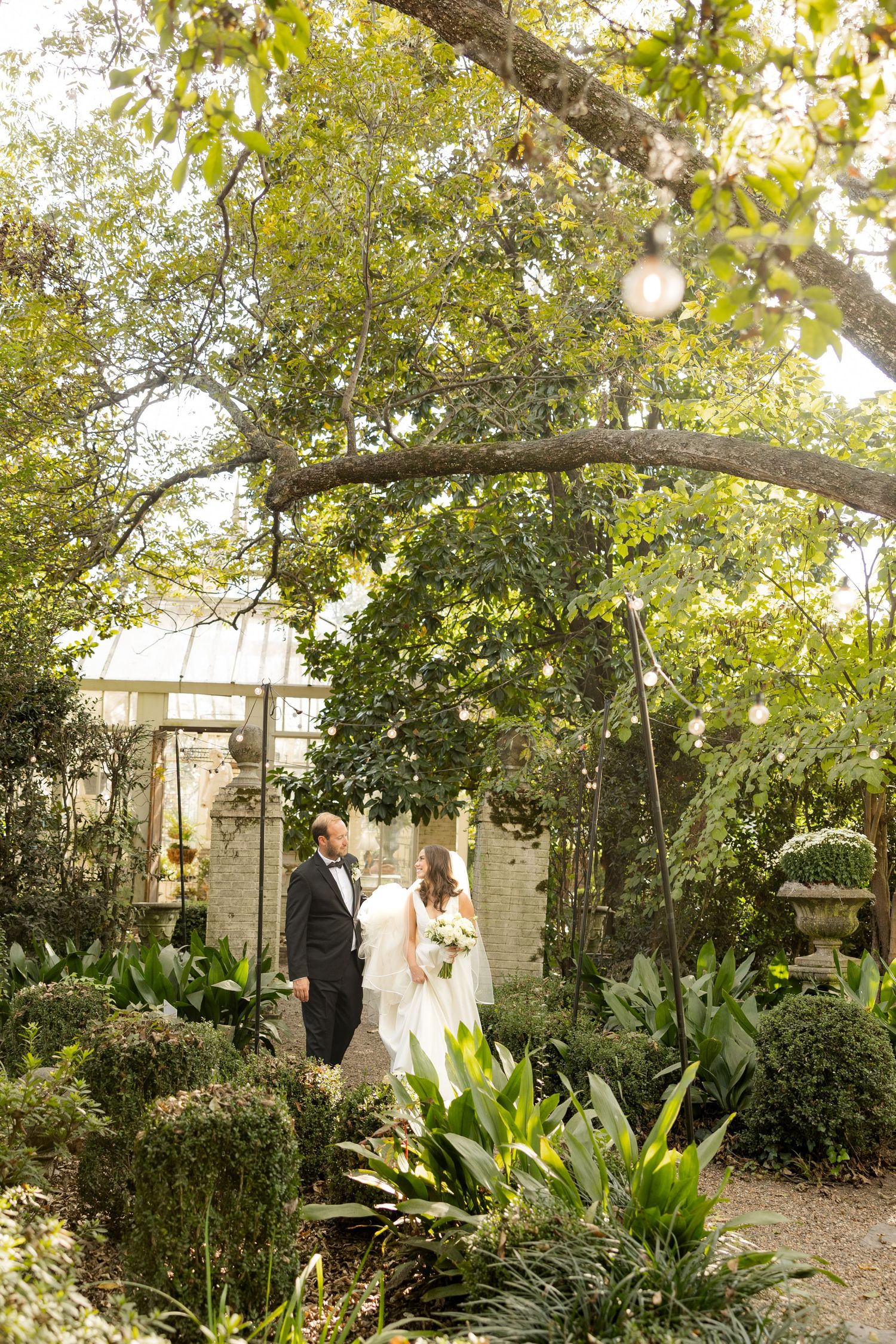 A romantic garden wedding scene with sunlight filtering through lush green trees and tropical plants.