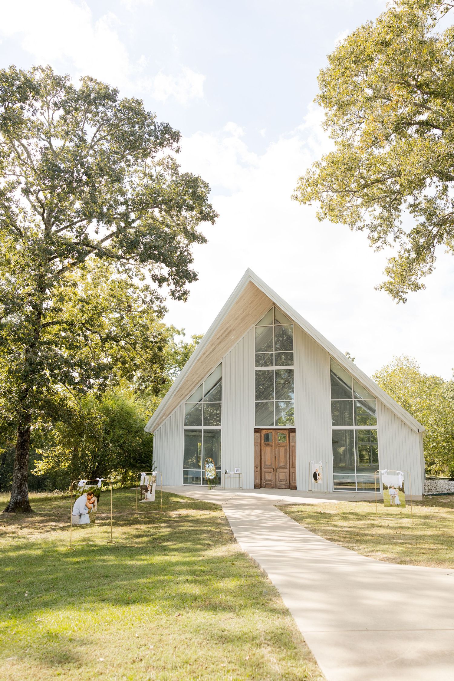Modern A-frame chapel with white exterior and large windows sits on a grassy hill surrounded by trees. Cold Springs Events.