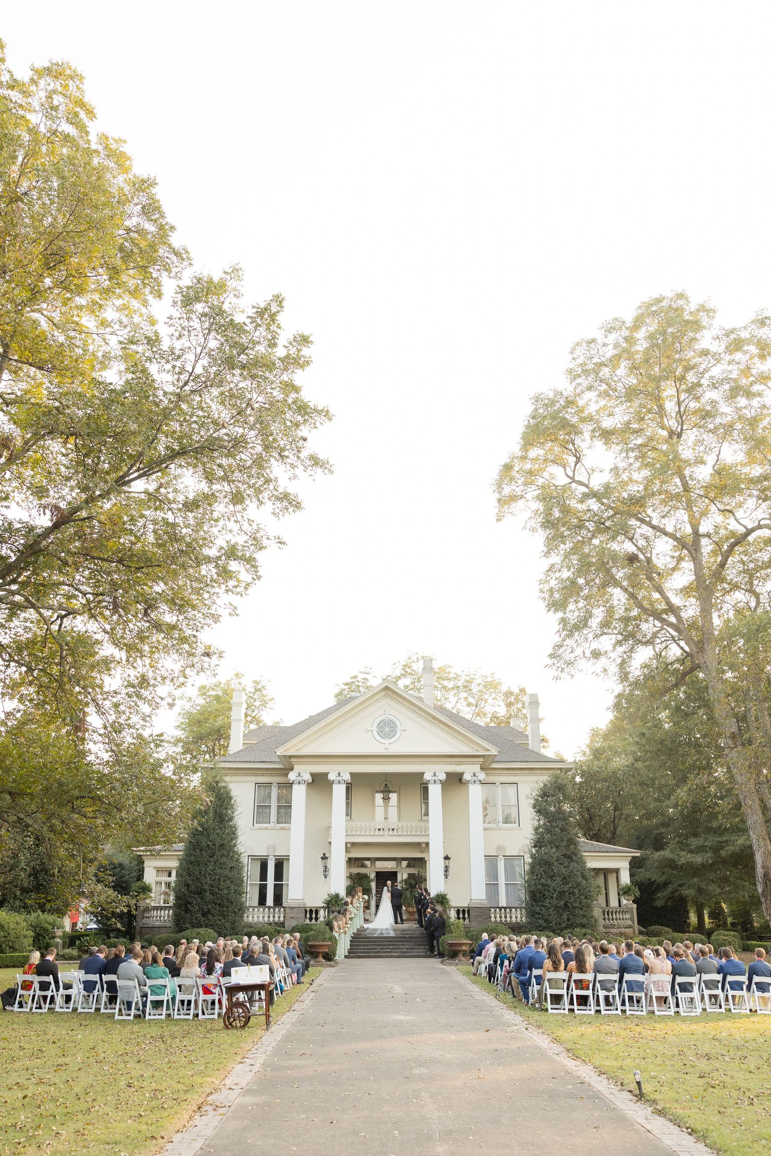 White colonial-style mansion set up for outdoor wedding ceremony with rows of chairs on the lawn.Marlgsate Plantation