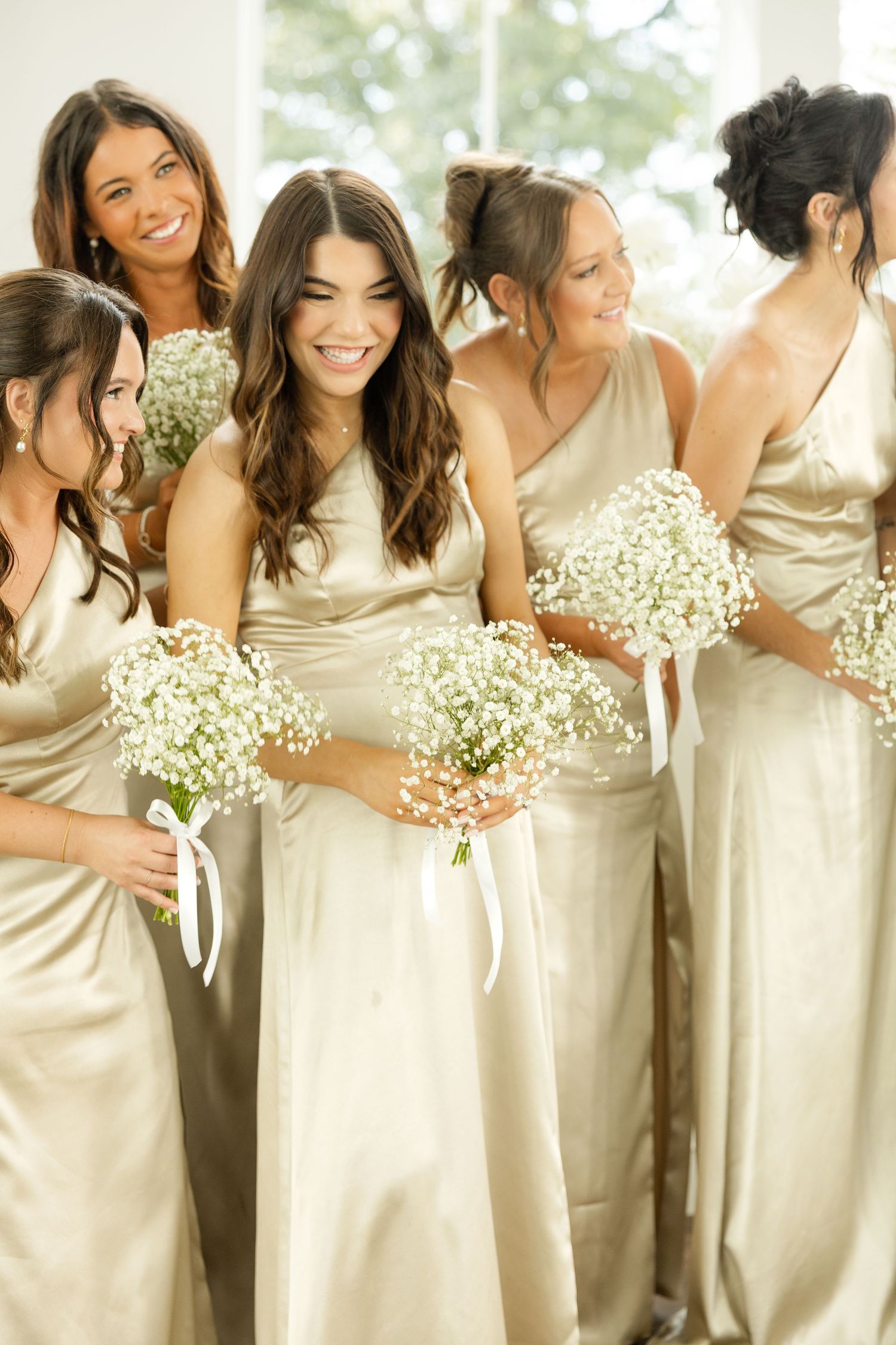 Bridesmaids in champagne-colored dresses holding baby's breath bouquets pose together.Grand at the Springs.