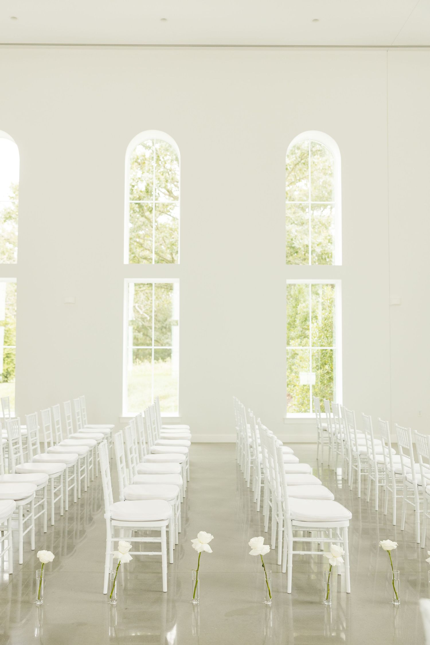 All-white wedding ceremony setup with rows of white chairs in a bright, sunlit room. Grand at the Springs.