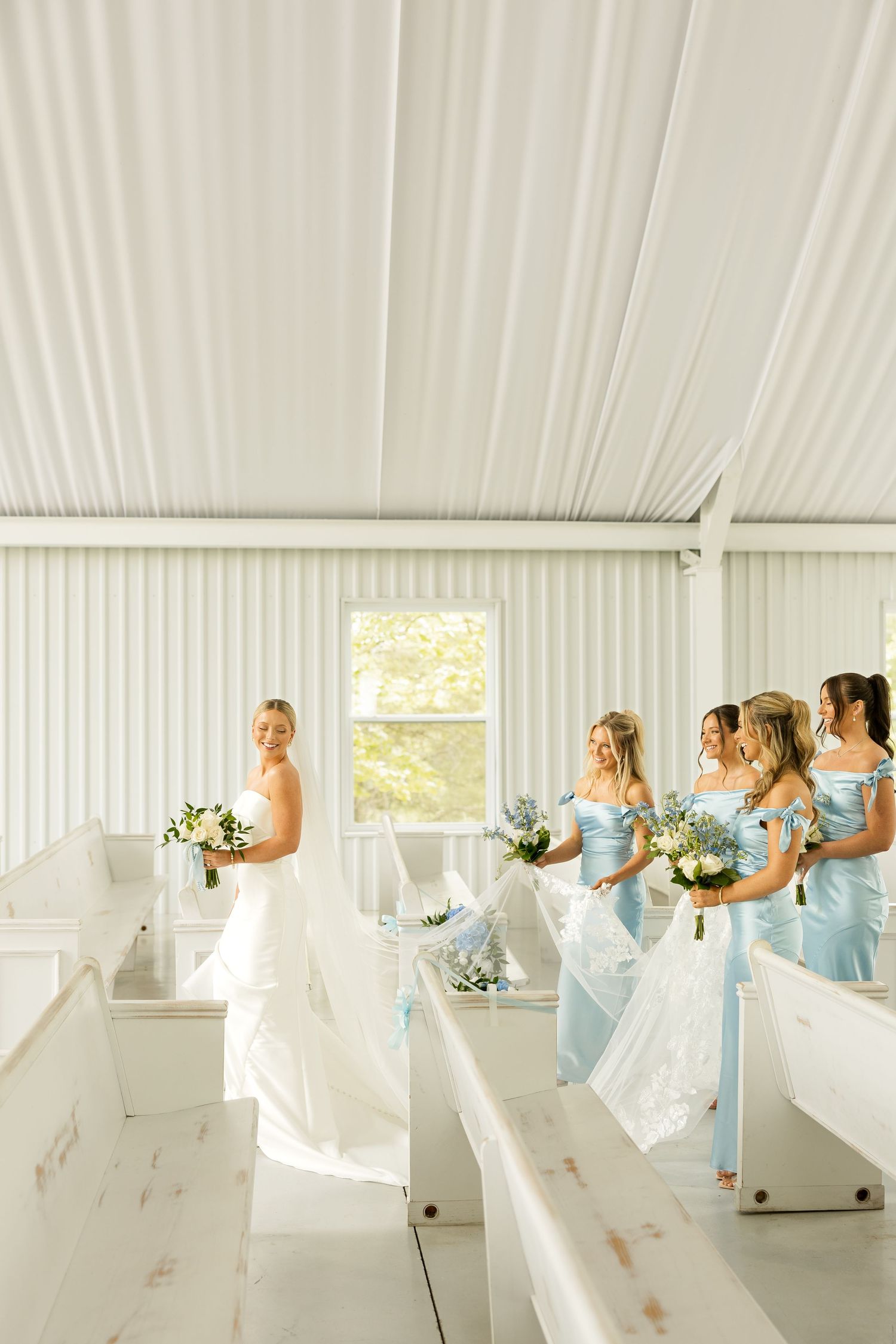 Bridesmaids in light blue dresses posing playfully in white church interior. Cold Springs Events