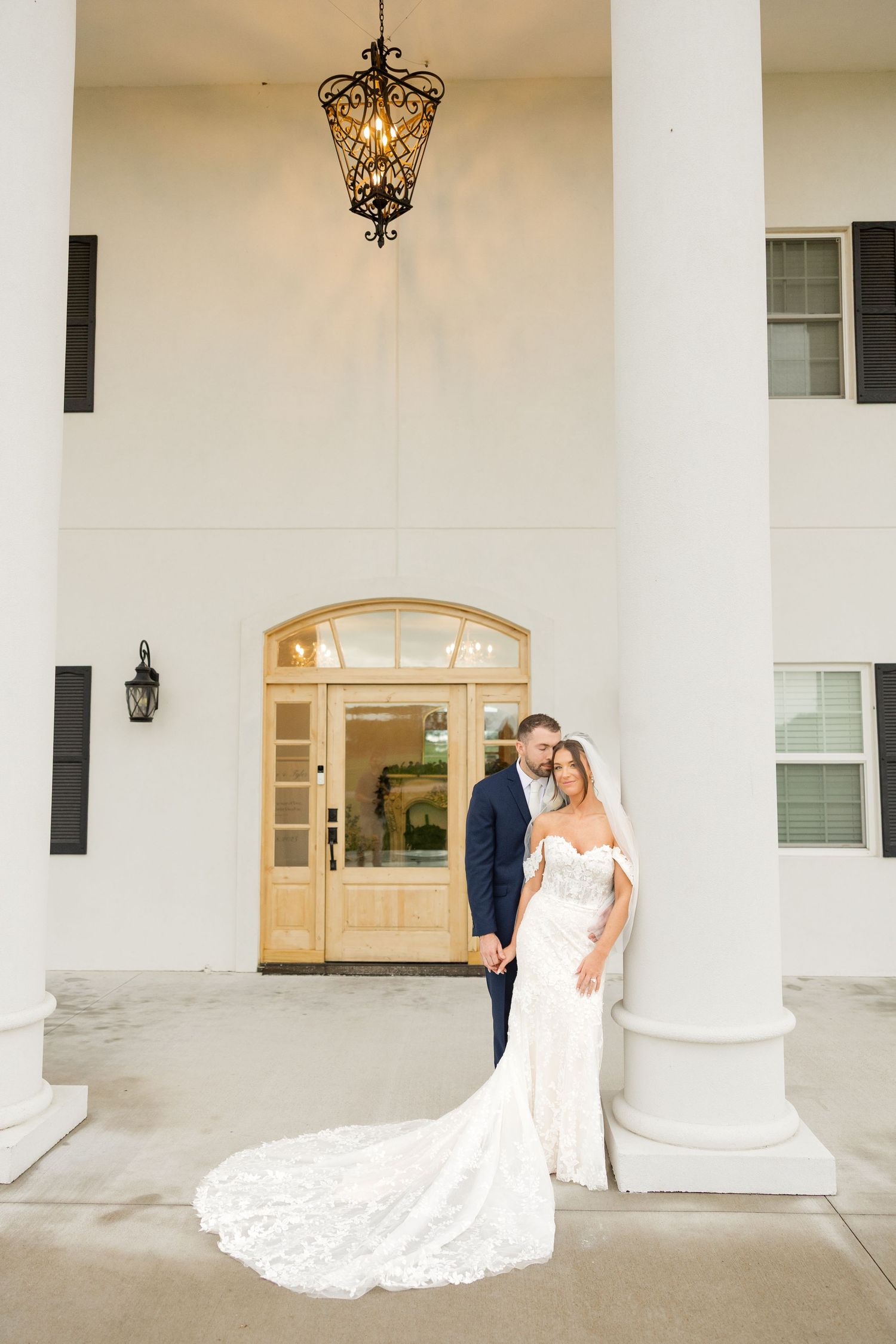 Elegant wedding portraits under white columned portico with hanging lanterns.