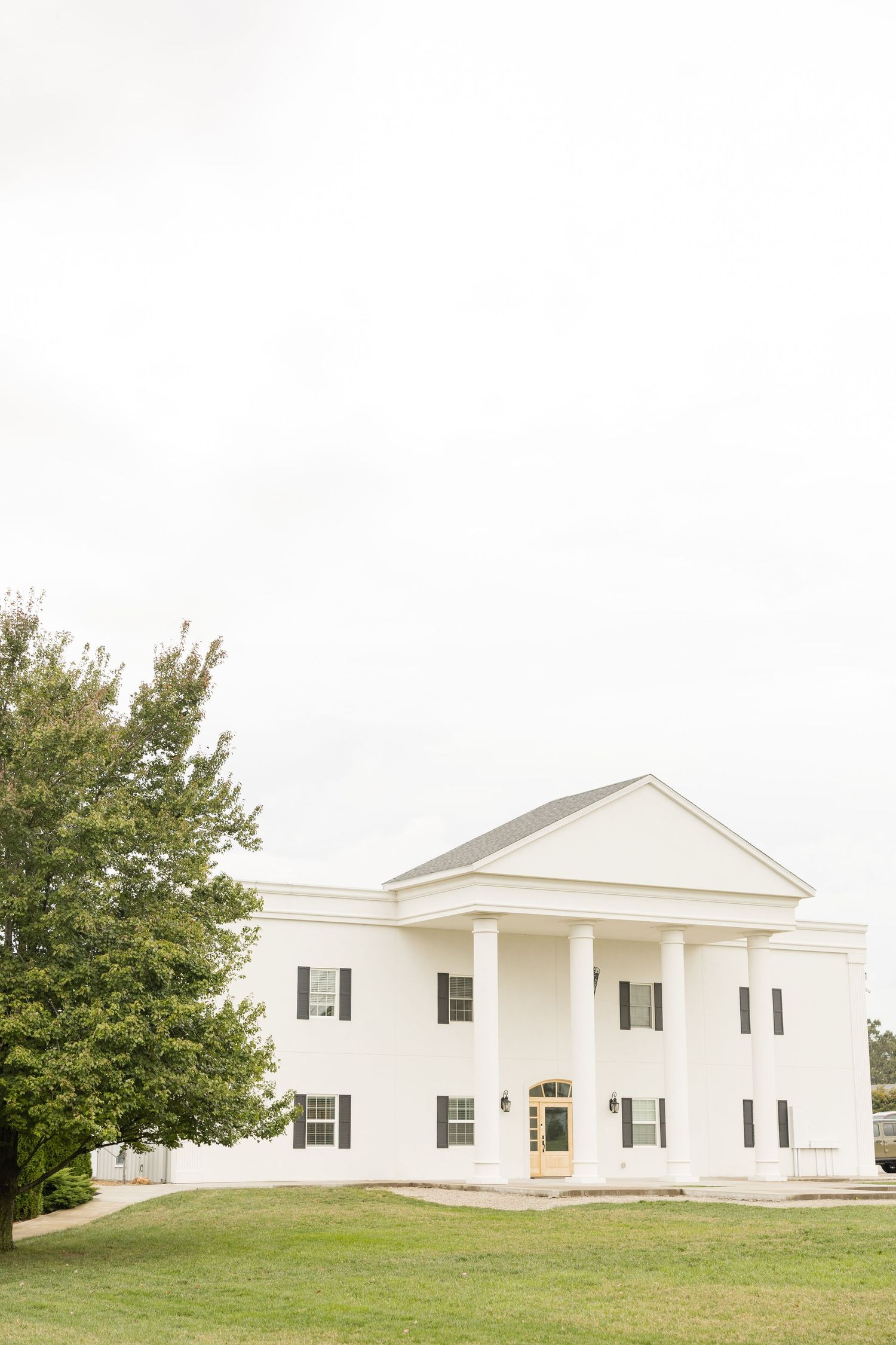 White church building with colonial-style architecture sits on a grassy hill surrounded by trees.