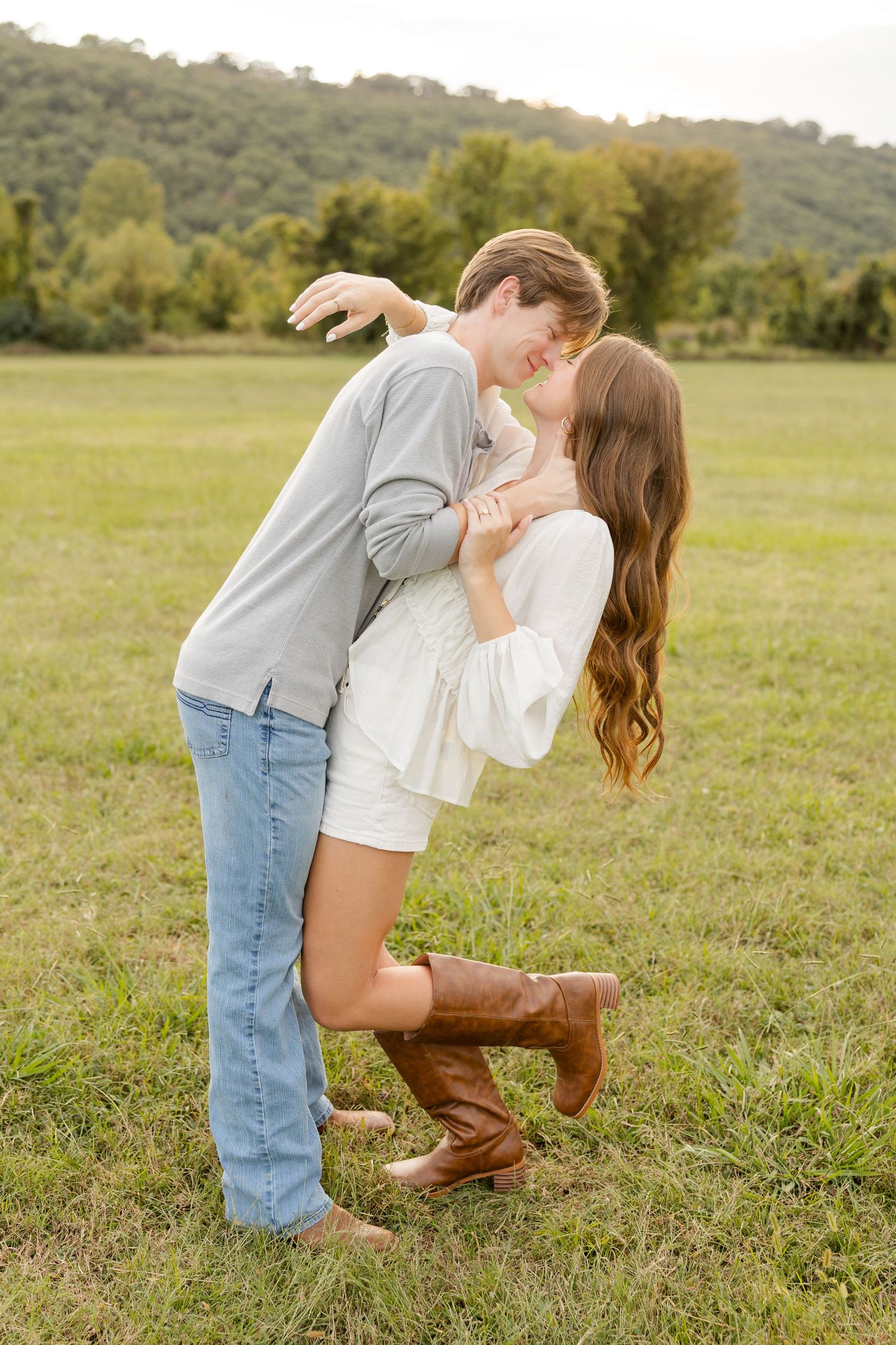 Couple embracing and sharing playful moments in a grassy field on a sunny afternoon.