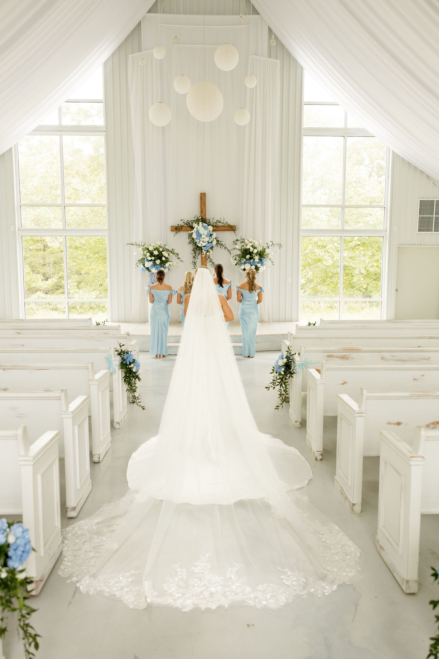 White wedding chapel interior with pews and draped fabric showing dramatic train of bridal gown.Cold Springs Events