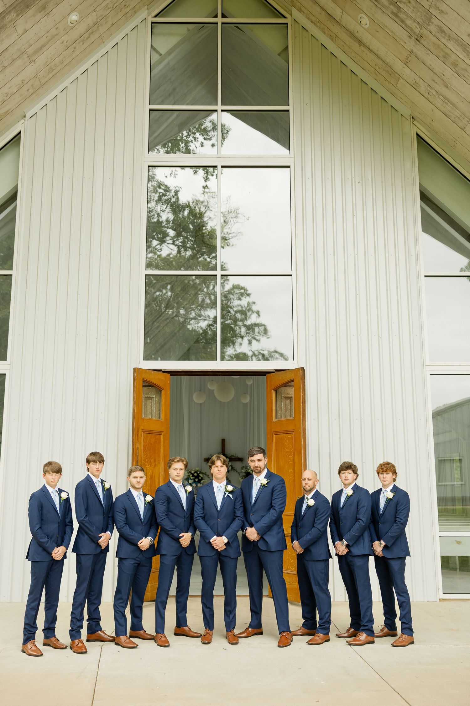 Wedding party in navy suits lined up for a creative group photo outside a white chapel at Cold Springs Events.