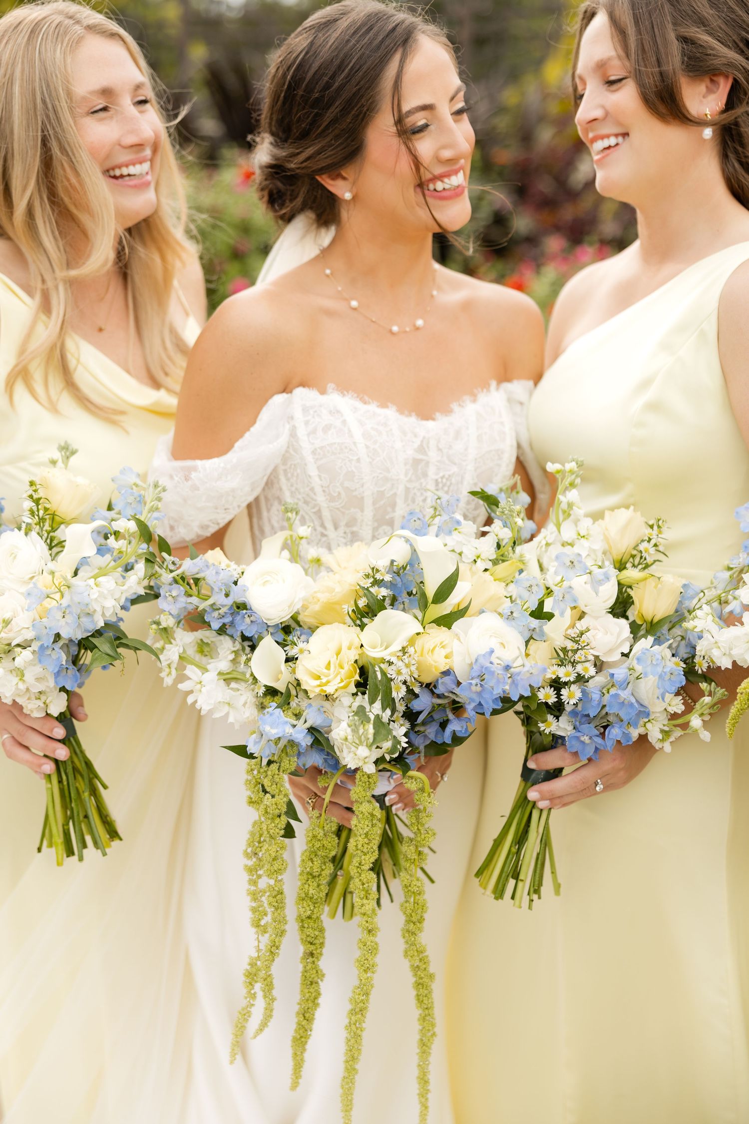 Bridesmaids in pale yellow dresses hold coordinated bouquets of white and blue flowers.Botanical Gardens of the Ozarks