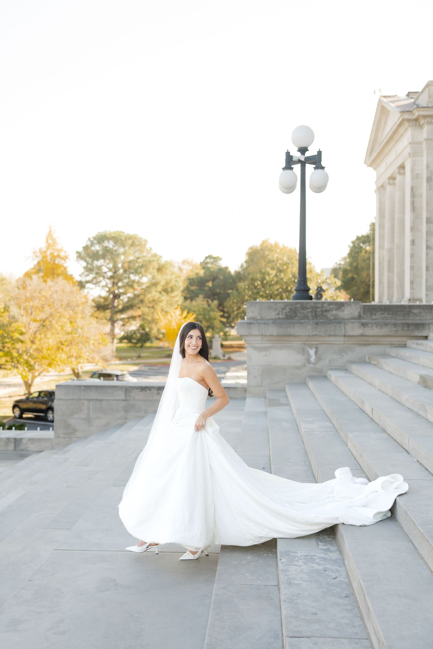 Bride in flowing white dress poses on stone steps during golden hour.