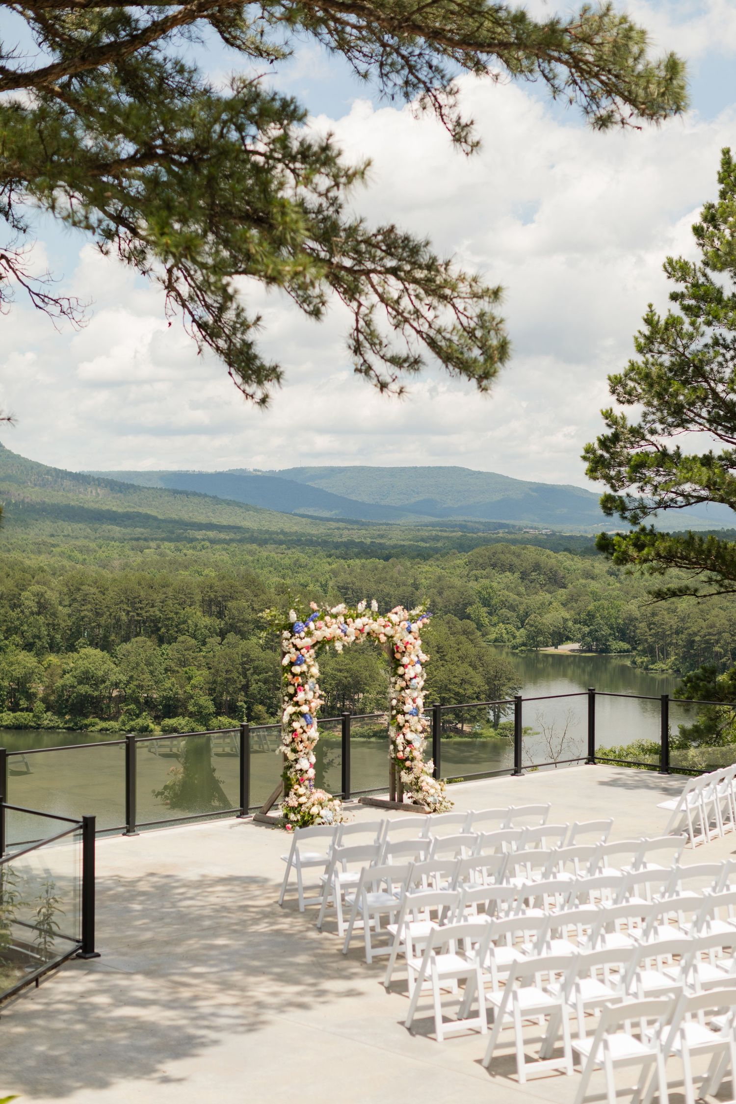 White chairs and floral arches arranged for an outdoor wedding ceremony overlooking a scenic mountain lake view.
