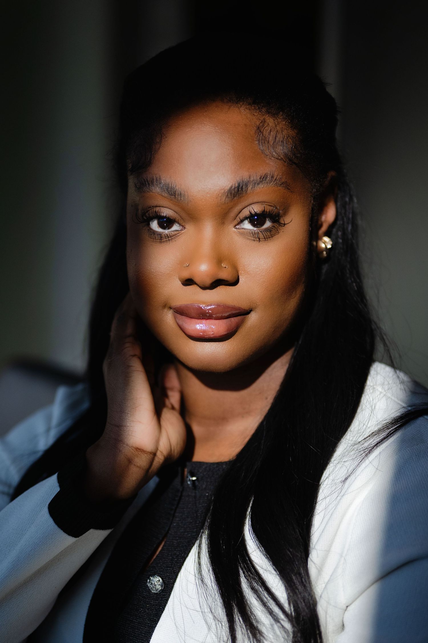 Close-up portrait of young woman with long black hair resting hand near face.