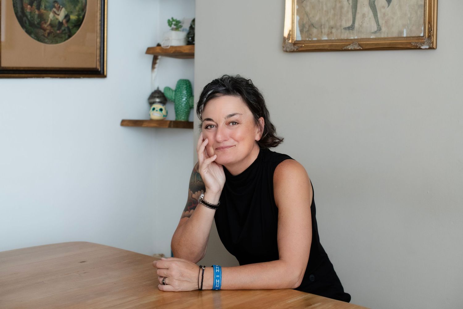 Woman in black sleeveless top sitting at wooden table in bright interior.