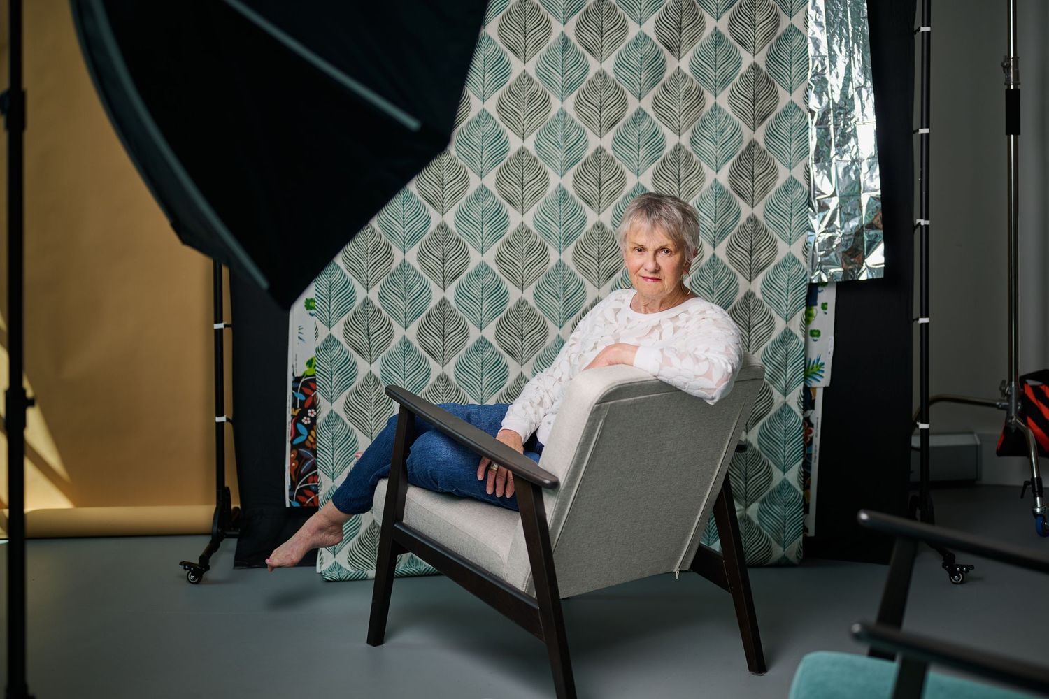 Woman sitting in a modern gray chair in a photography studio with a decorative green backdrop.