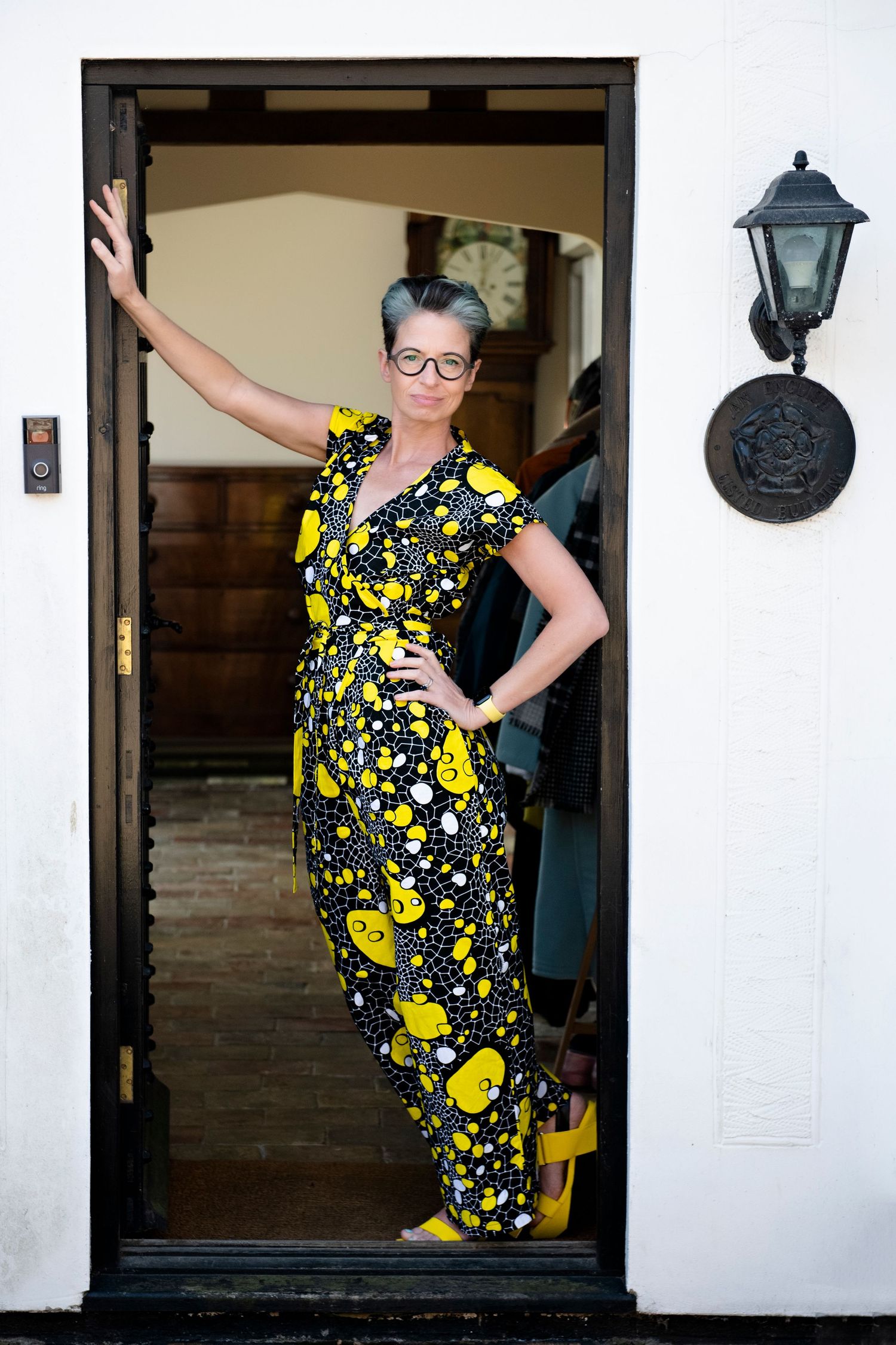 Woman in a black and yellow floral jumpsuit posing confidently in an open doorway with yellow shoes.