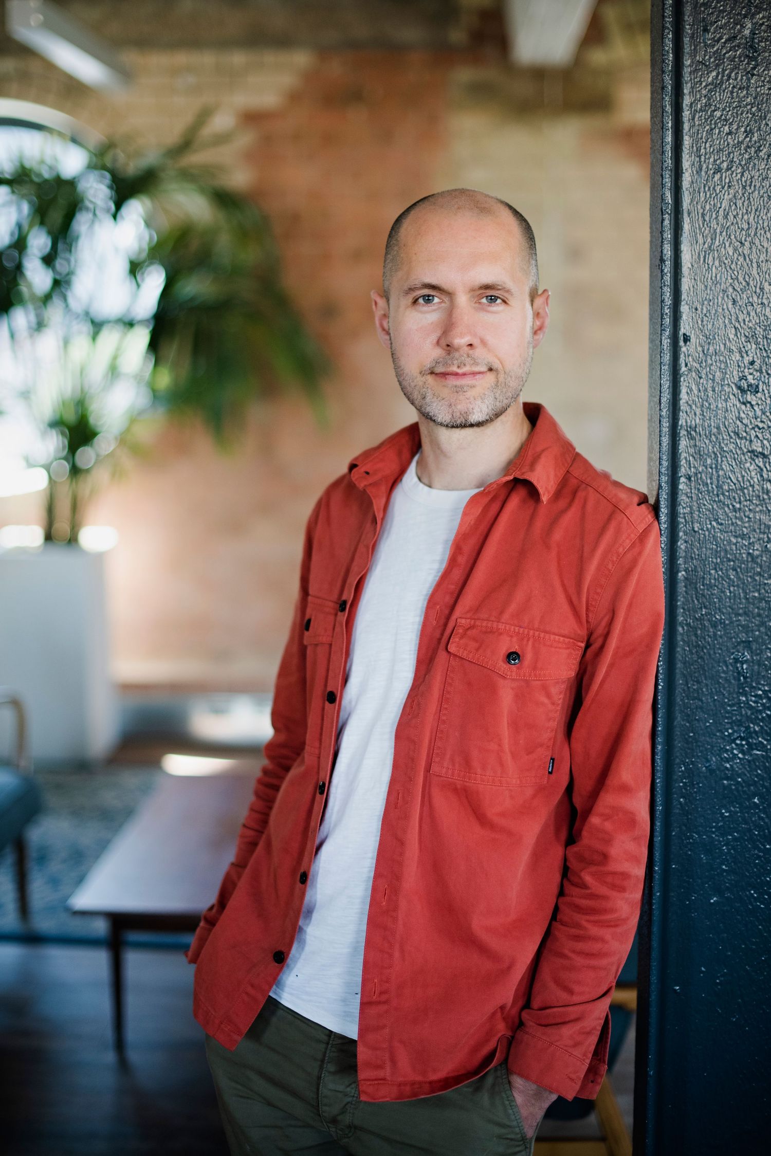 Man in red jacket leaning against dark pillar in modern brick interior.