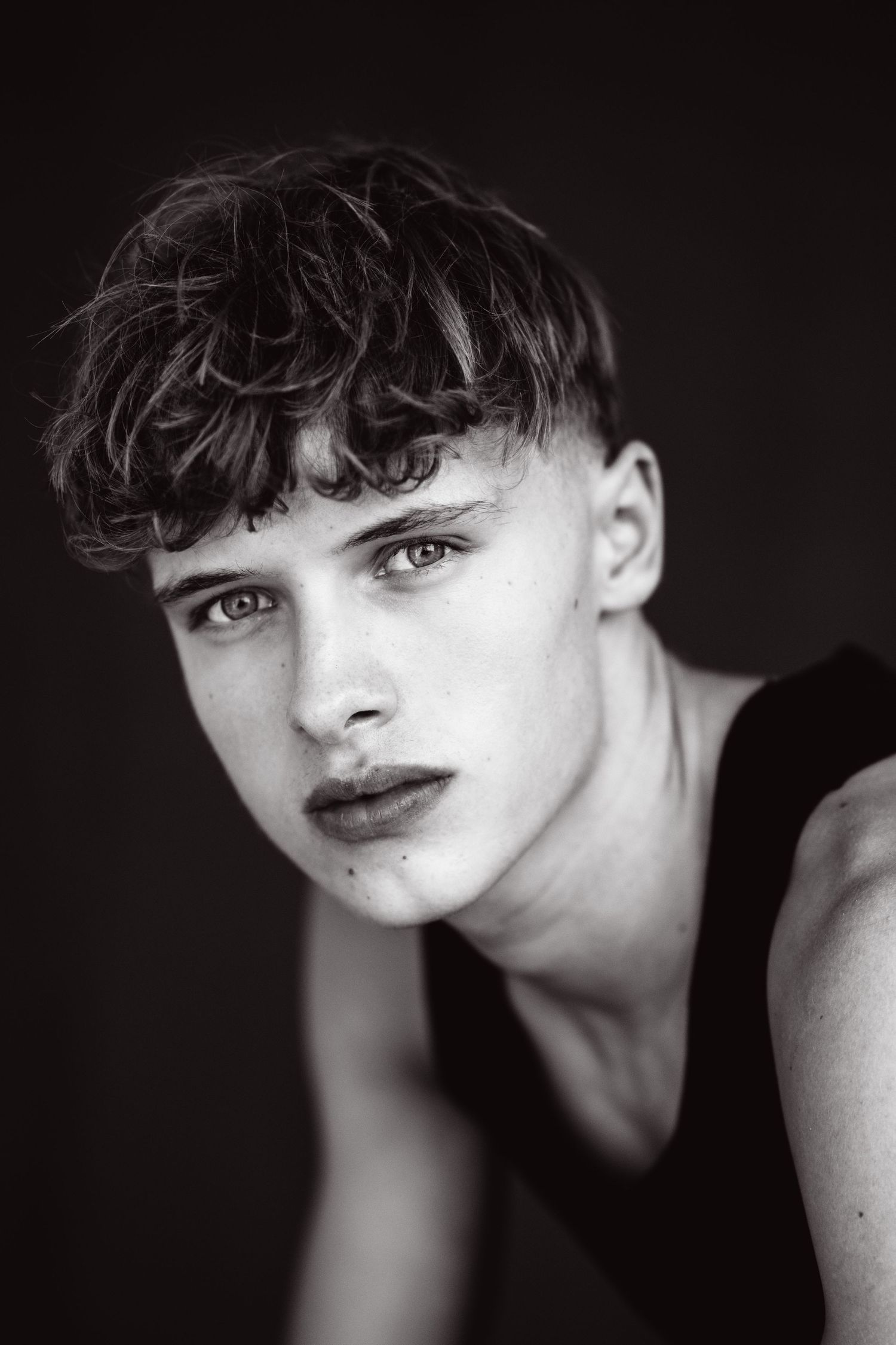Black and white portrait of a young male model with curly hair wearing a black tank top.