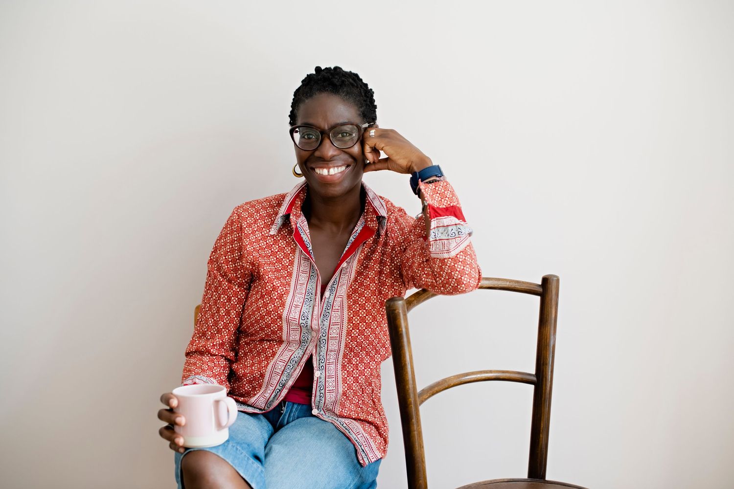 Smiling woman in red shirt sitting on chair holding mug.