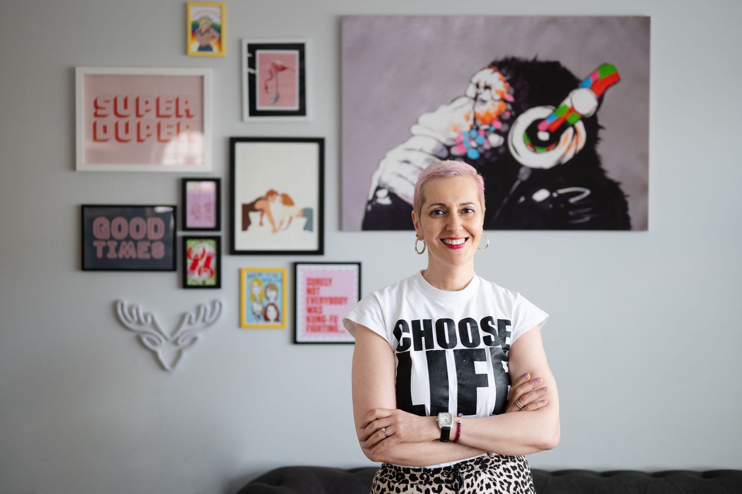 Smiling woman in Choose Life t-shirt standing in front of colorful gallery wall with pop art prints.