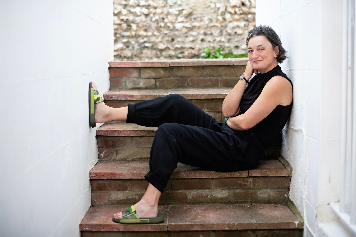 Woman in black outfit sitting relaxed on rustic stone steps outdoors.