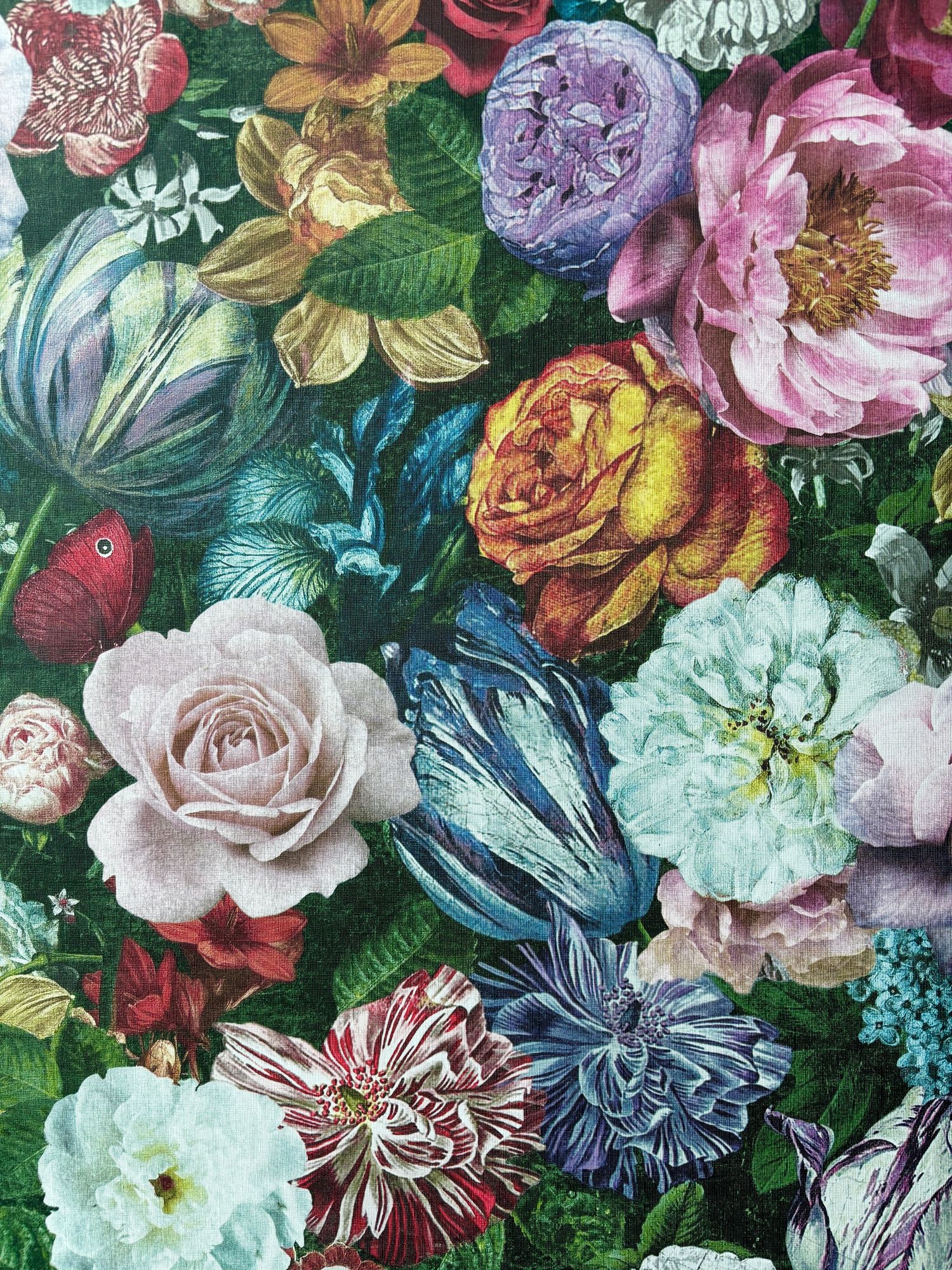 Close-up of a vibrant floral fabric print featuring roses, peonies, and butterflies in rich, saturated colors on a green background.