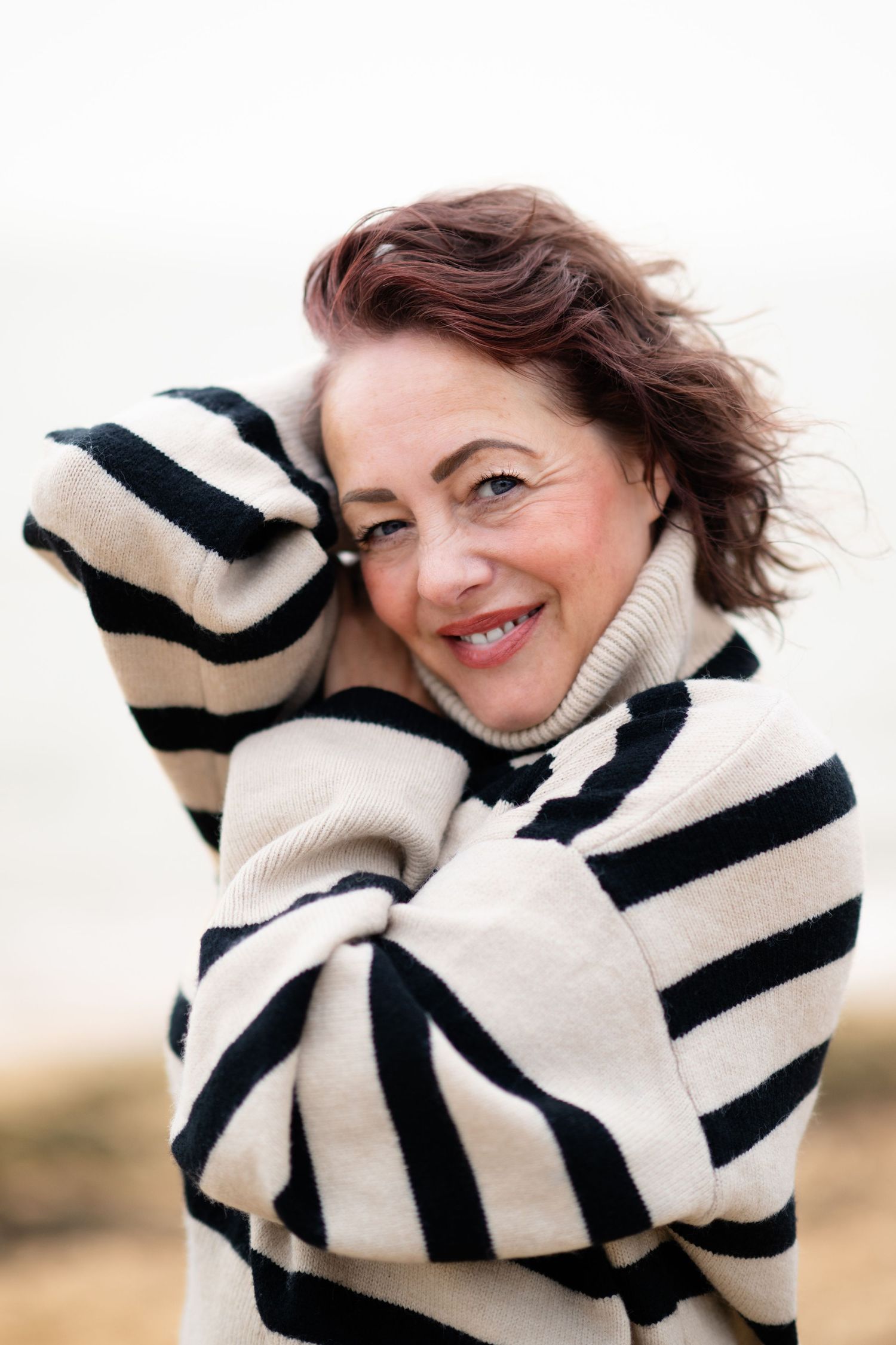 Smiling woman in black and white striped sweater outdoors with wind blowing her hair.
