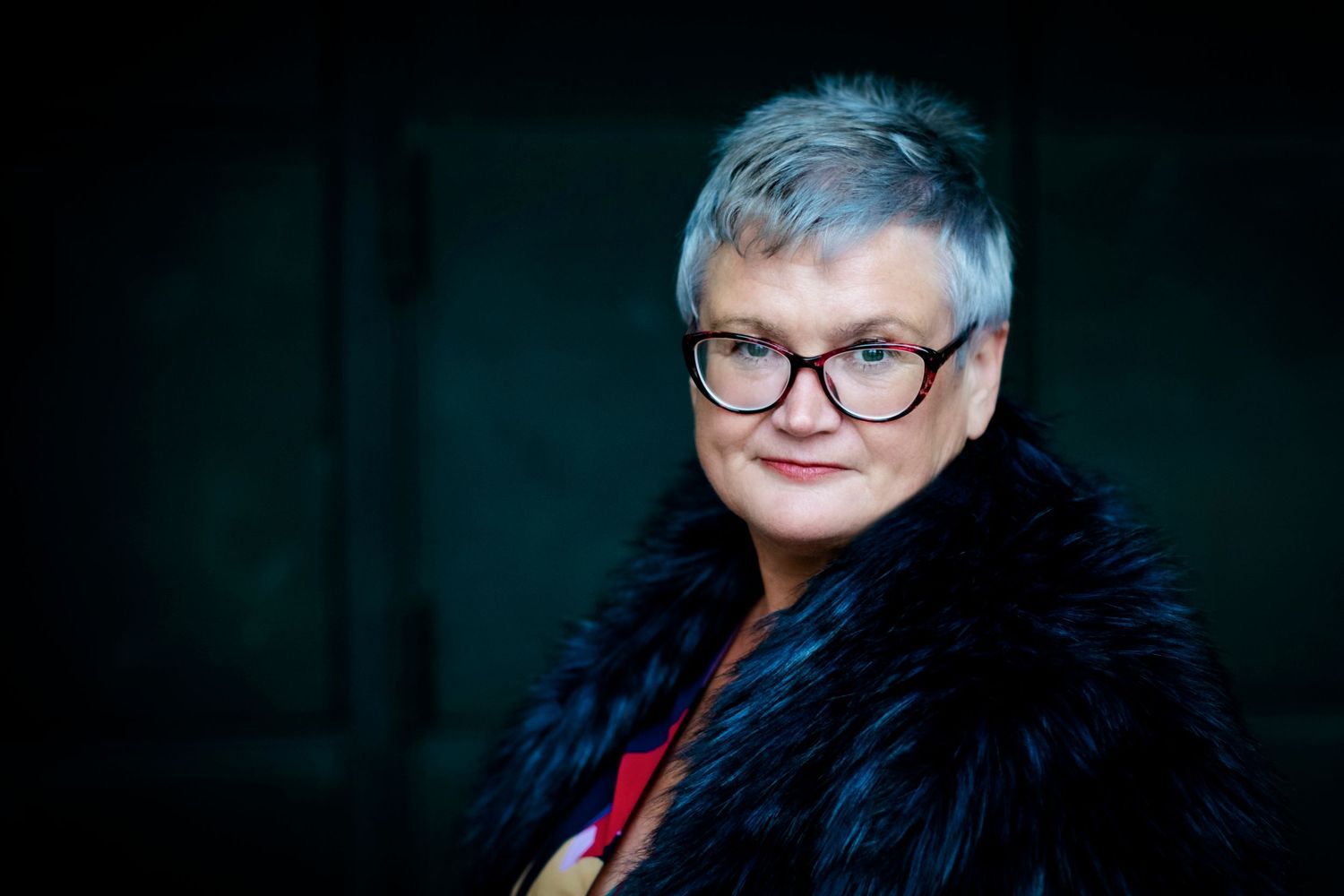 Senior woman with gray hair and glasses wearing fur collar coat.