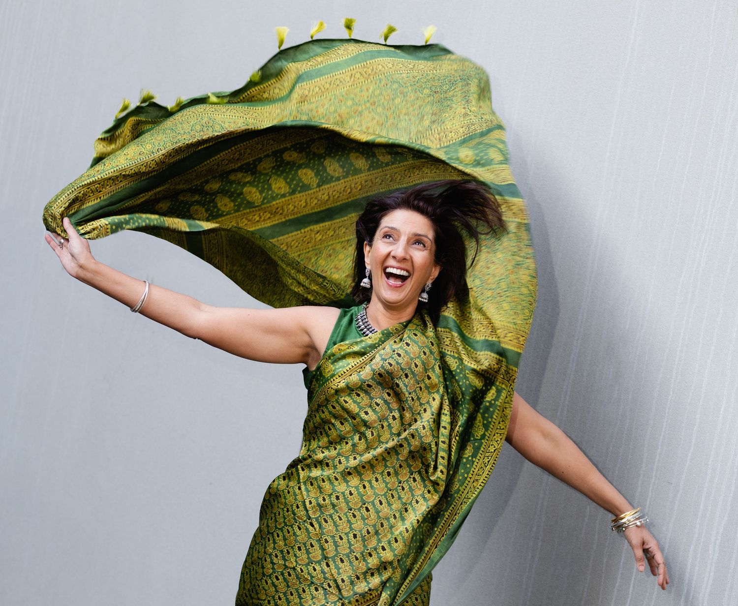 Joyful woman in a flowing green sari twirls elegantly against a light gray background.
