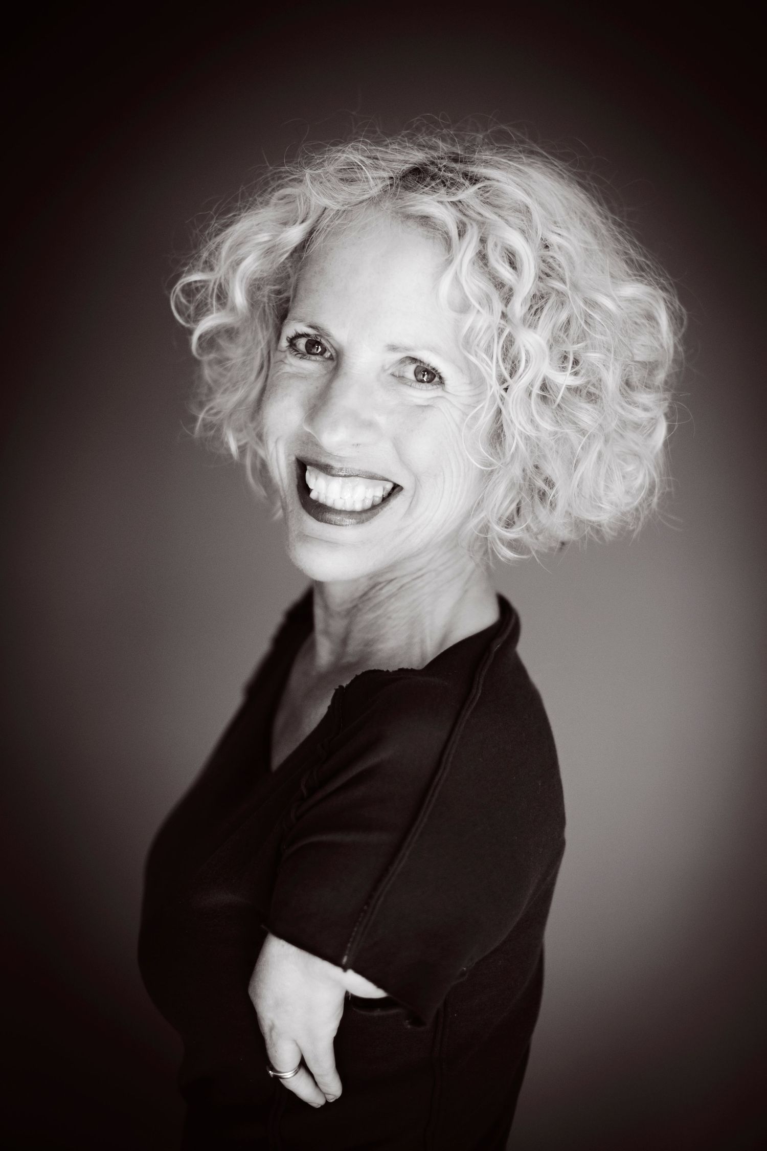 Black and white portrait of curly blonde woman smiling with arms crossed.