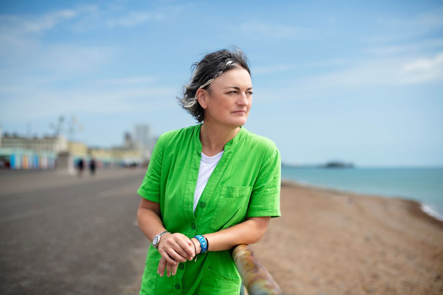 Woman in bright green top standing on a beach with pier in background.