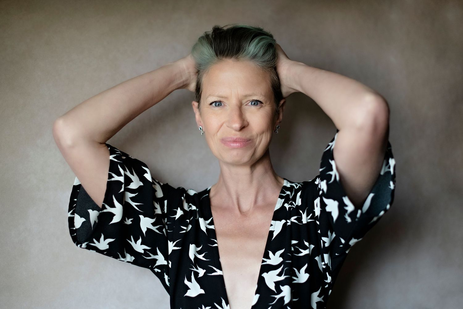 Woman with short teal hair in a black and white bird-print wrap dress holding her hair up.