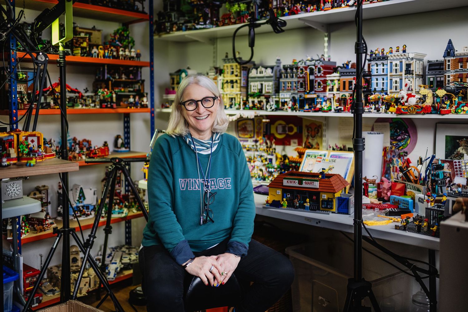 Woman with glasses smiling in a room filled with colorful LEGO sets and displays.