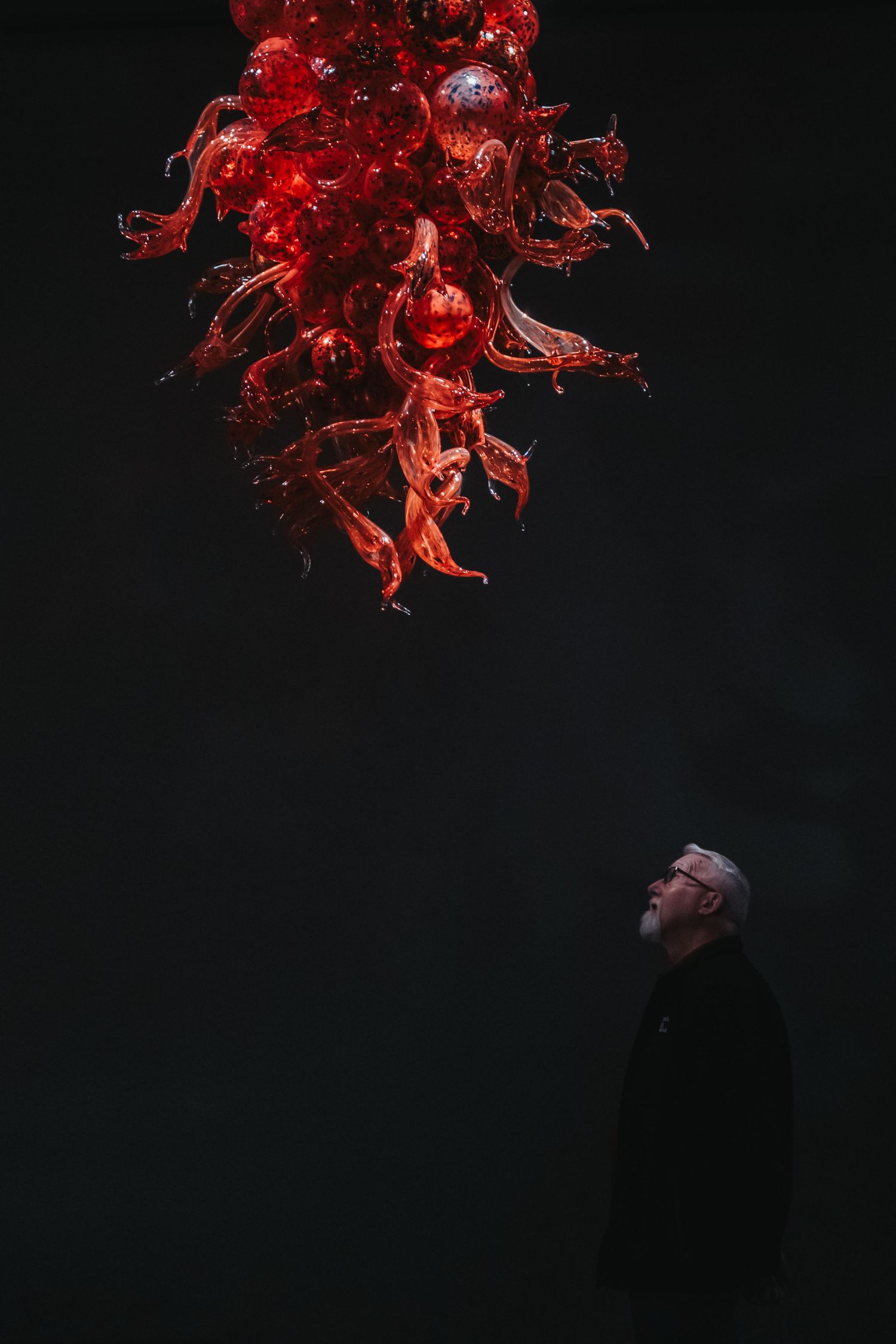 Dramatic red glass chandelier sculpture against dark background.