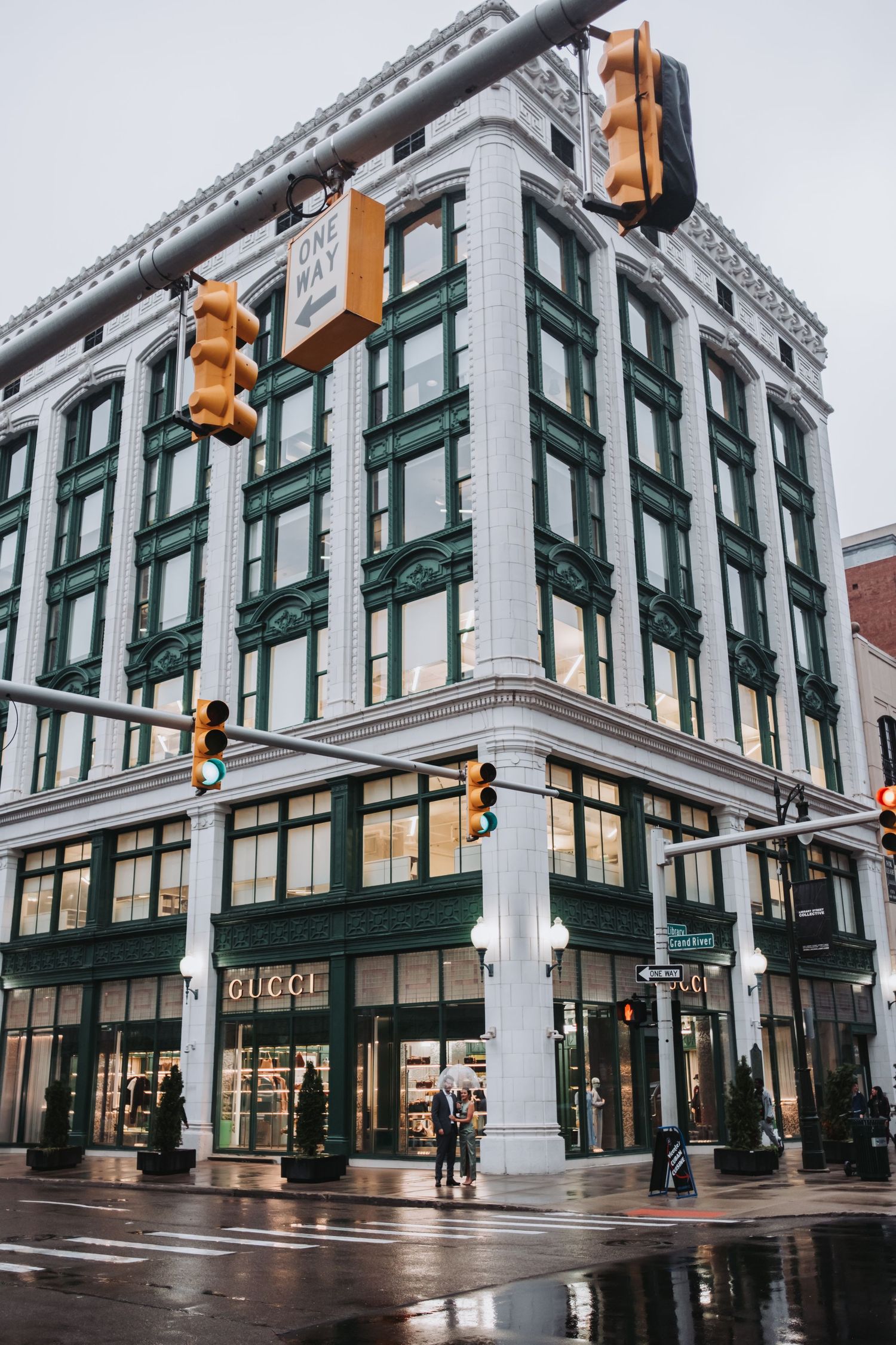 Gucci luxury store on a rainy street corner with green facade, traffic lights, and wet reflective pavement.