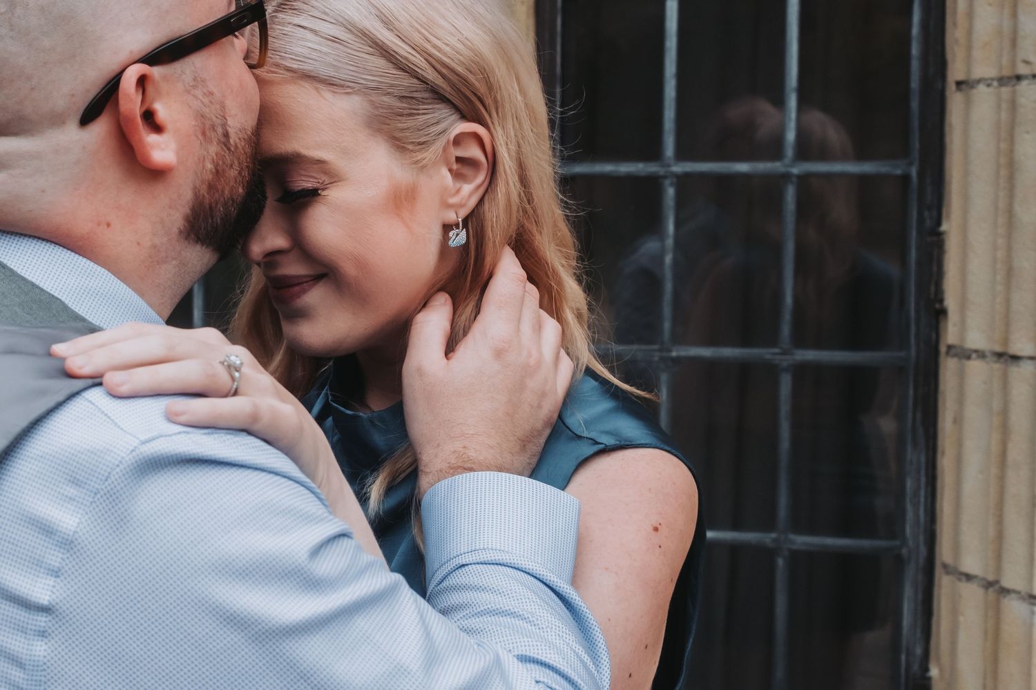 A romantic couple shares an intimate moment near a stone building exterior.