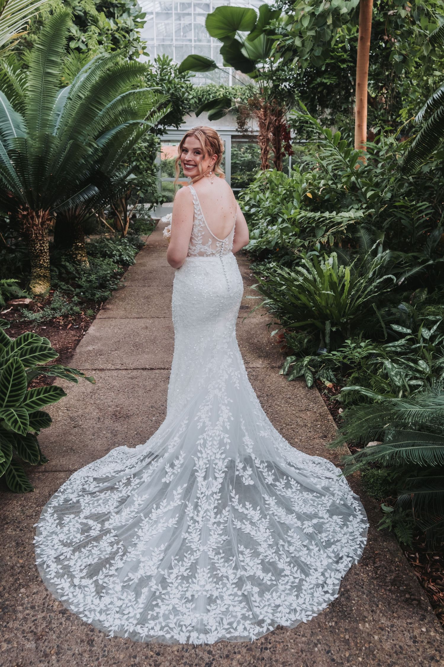 Beautiful lace wedding dress with long train photographed in a botanical garden setting.
