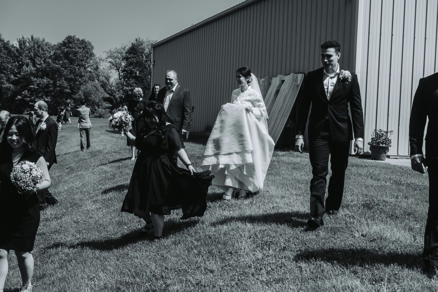 Wedding guests walking across a grassy lawn outside a large industrial-style building.