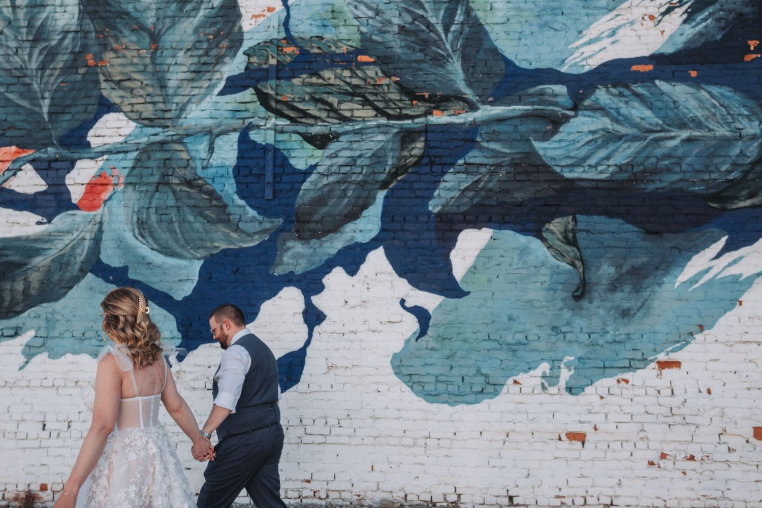 A painted mural featuring large tropical leaves in shades of blue on a white brick wall.