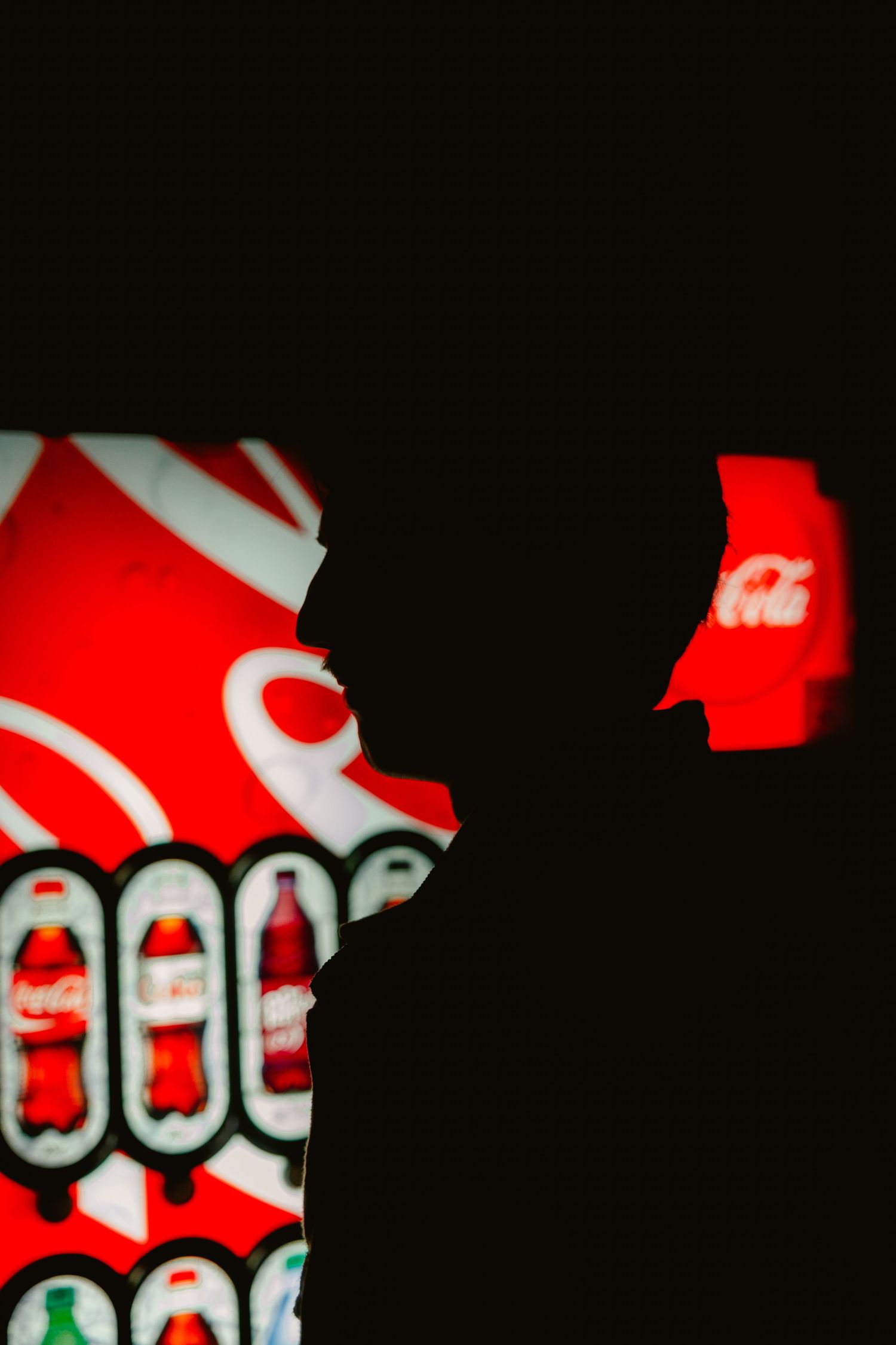 Silhouette of a person against a glowing Coca-Cola advertisement display in a dark setting.