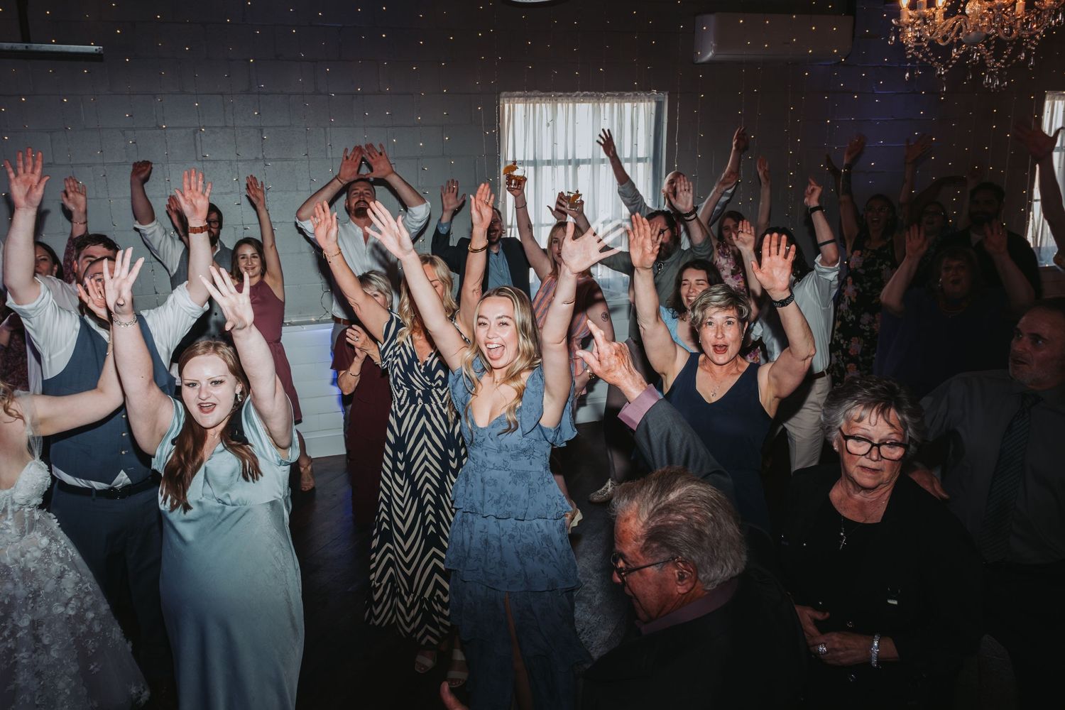 Party guests with raised hands dancing and celebrating at a dimly lit reception venue.