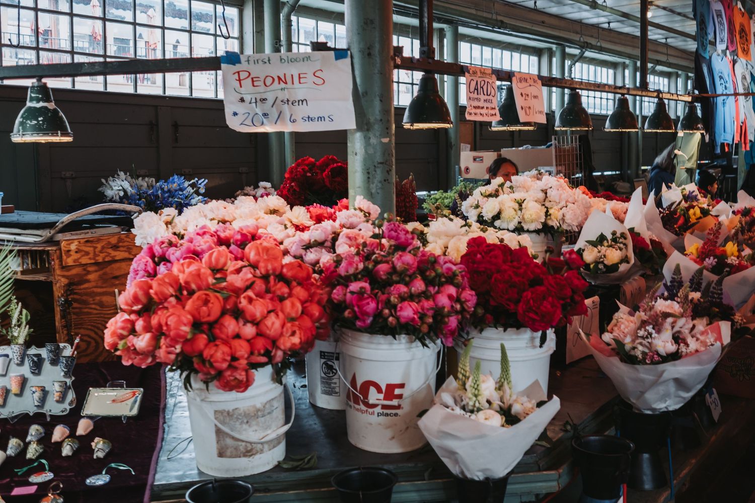 Colorful peonies and roses displayed in white buckets at a vibrant flower market stall indoors.
