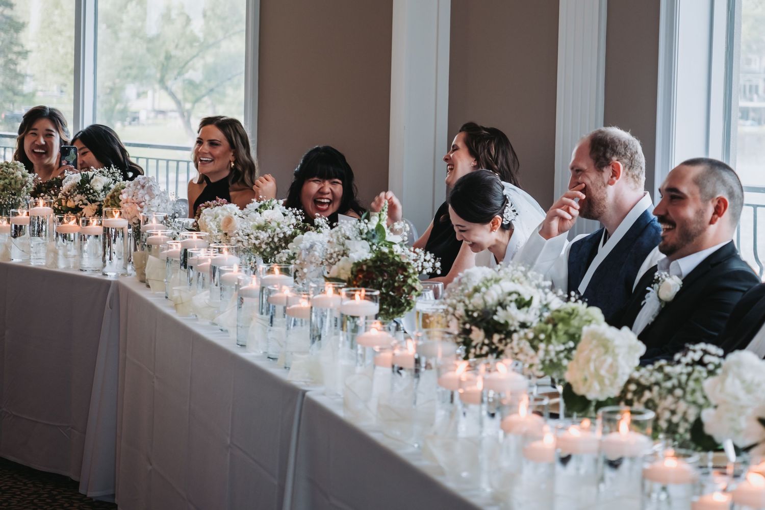Elegant wedding reception table setting with white floral centerpieces and glowing candles.