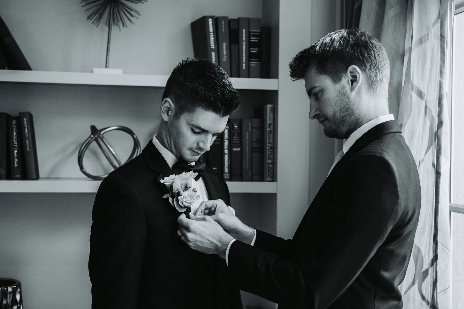 Groomsmen in black suits share emotional moment during wedding preparations.