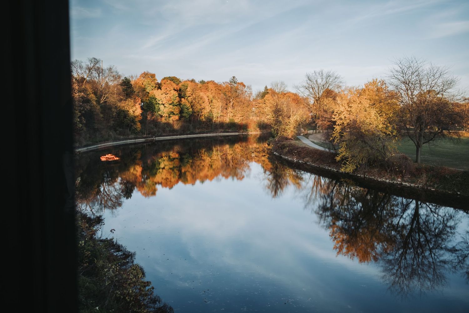 Autumn trees with golden foliage reflecting on a calm lake under a blue sky in a serene park landscape.