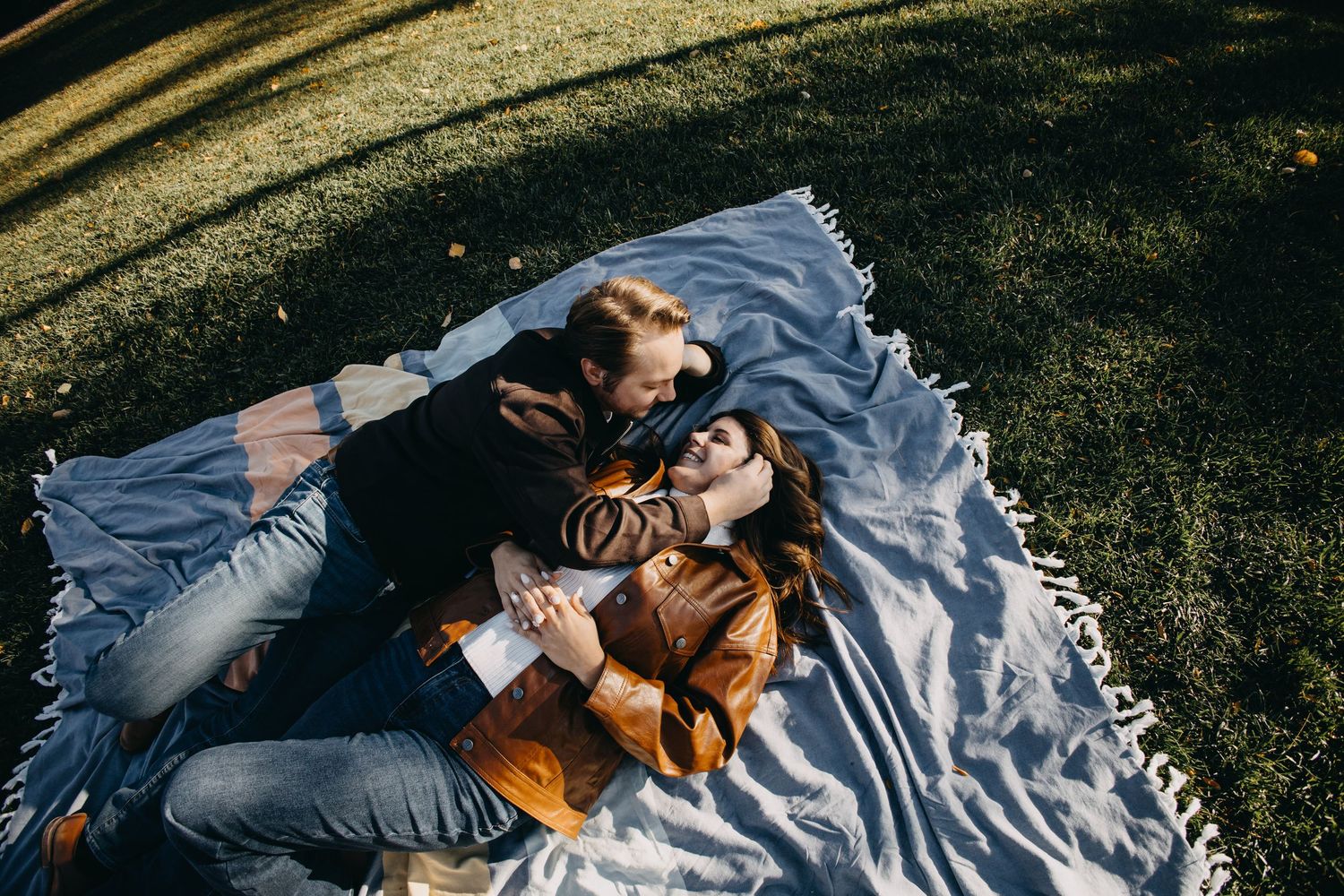 Couple lying on a blanket in a park, sharing a romantic moment outdoors on a sunny autumn day.