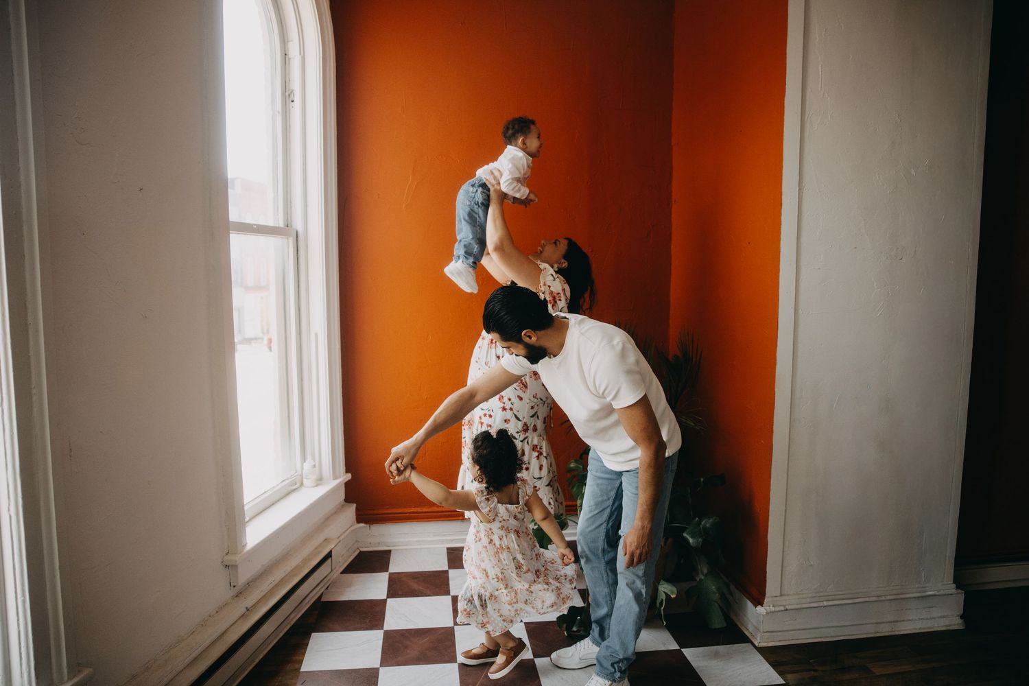 Family playing together in a room with orange walls and checkered floors near a bright window.