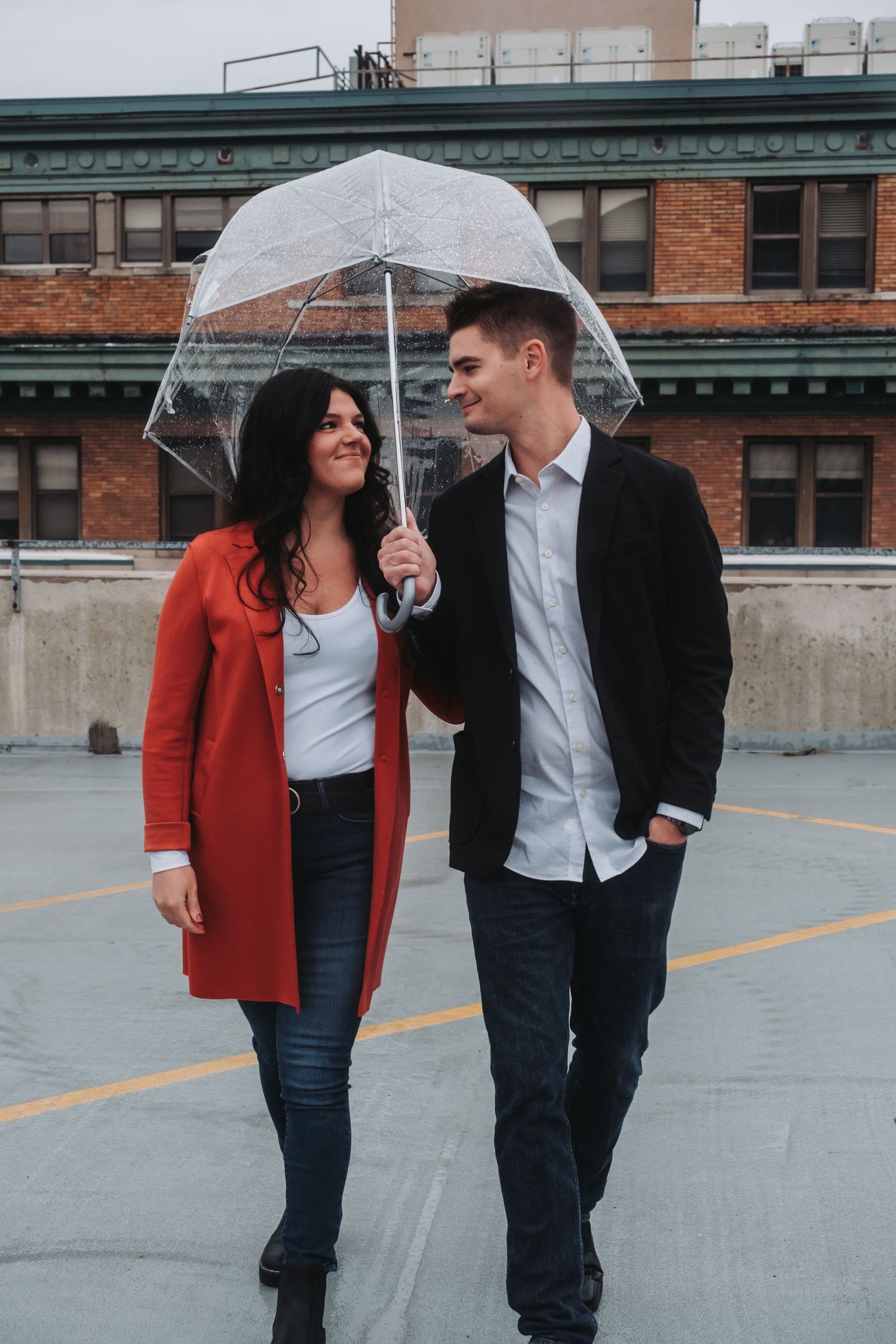 Couple sharing umbrella and romantic moments on rainy rooftop in urban setting.