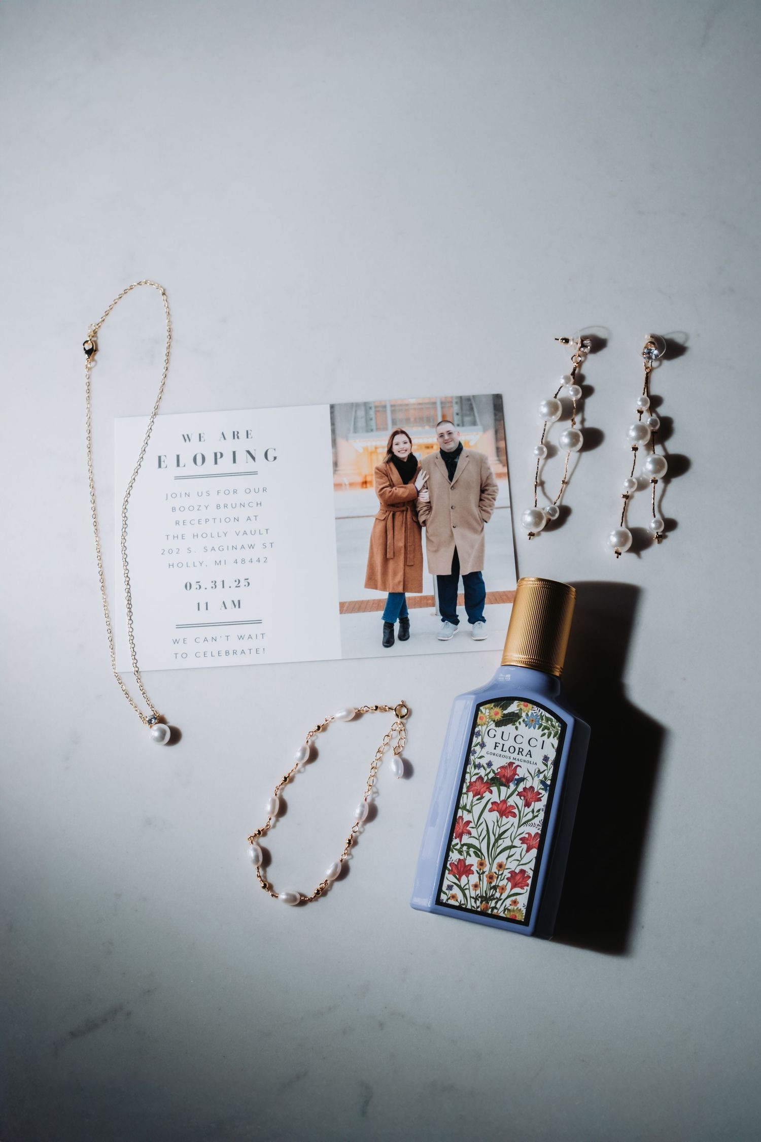 Flatlay of jewelry, perfume bottle and wedding invitation card on light gray background.